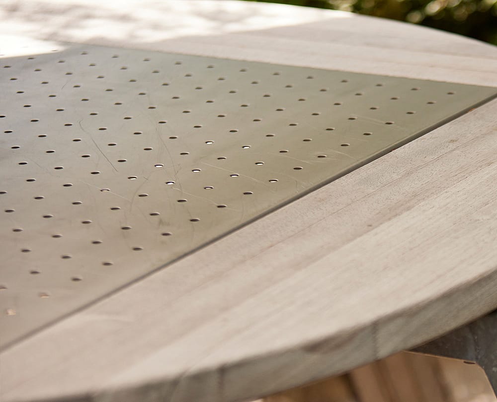 Gros plan sur un plateau de table en bois avec un insert métallique perforé, montrant des rayures de surface et des détails du matériau.
