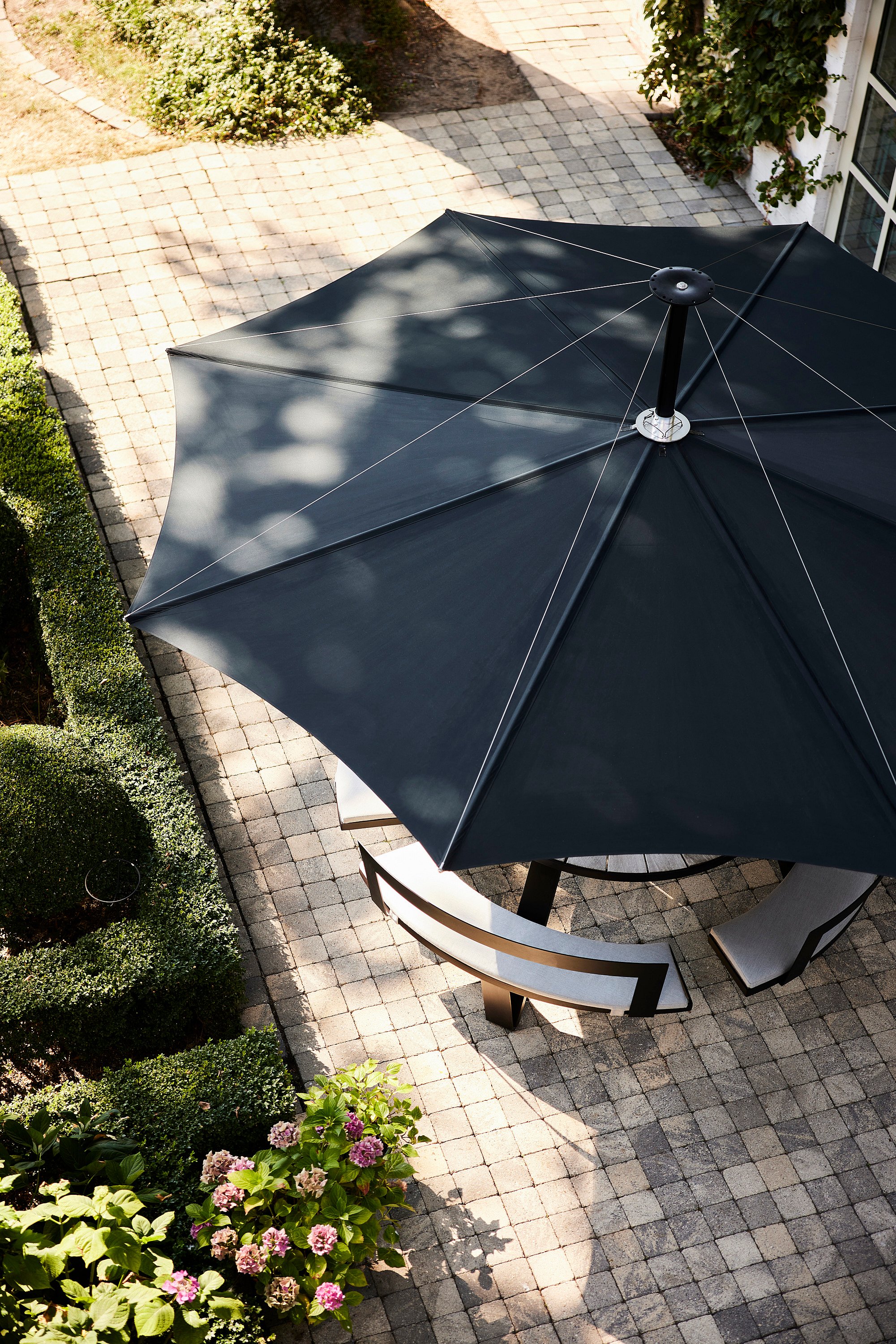 Aerial view of a dark blue Inumbra parasol shading a curved bench in a garden.