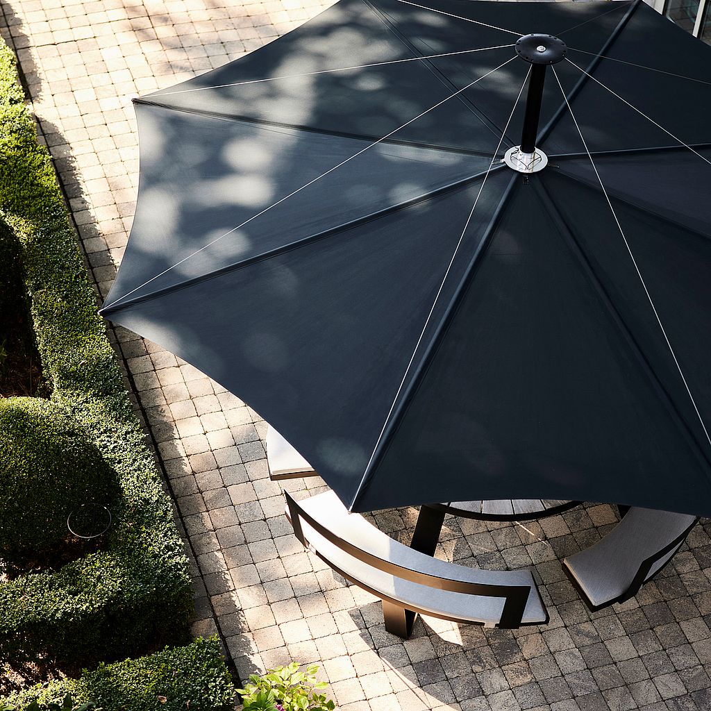 Aerial view of a dark blue Inumbra parasol shading a curved bench in a garden.