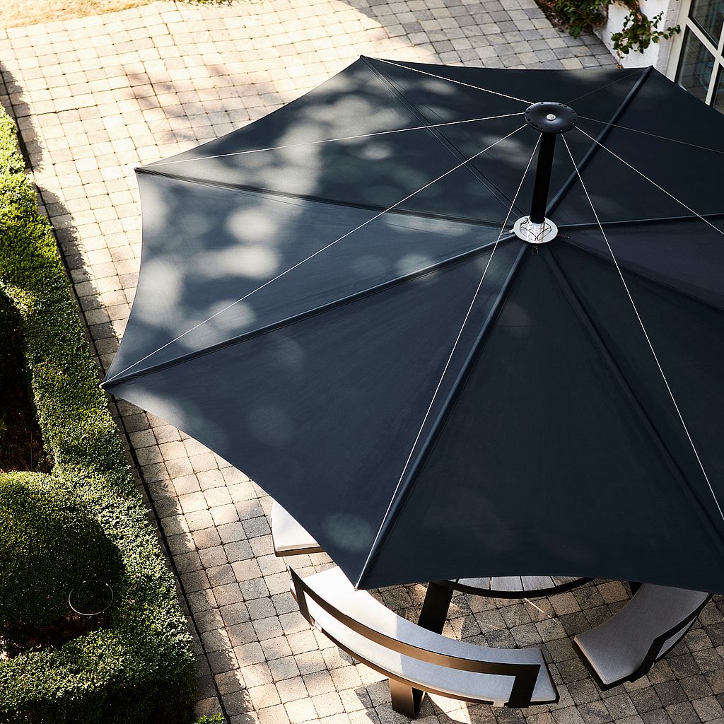 Aerial view of a dark blue Inumbra parasol shading a curved bench in a garden.