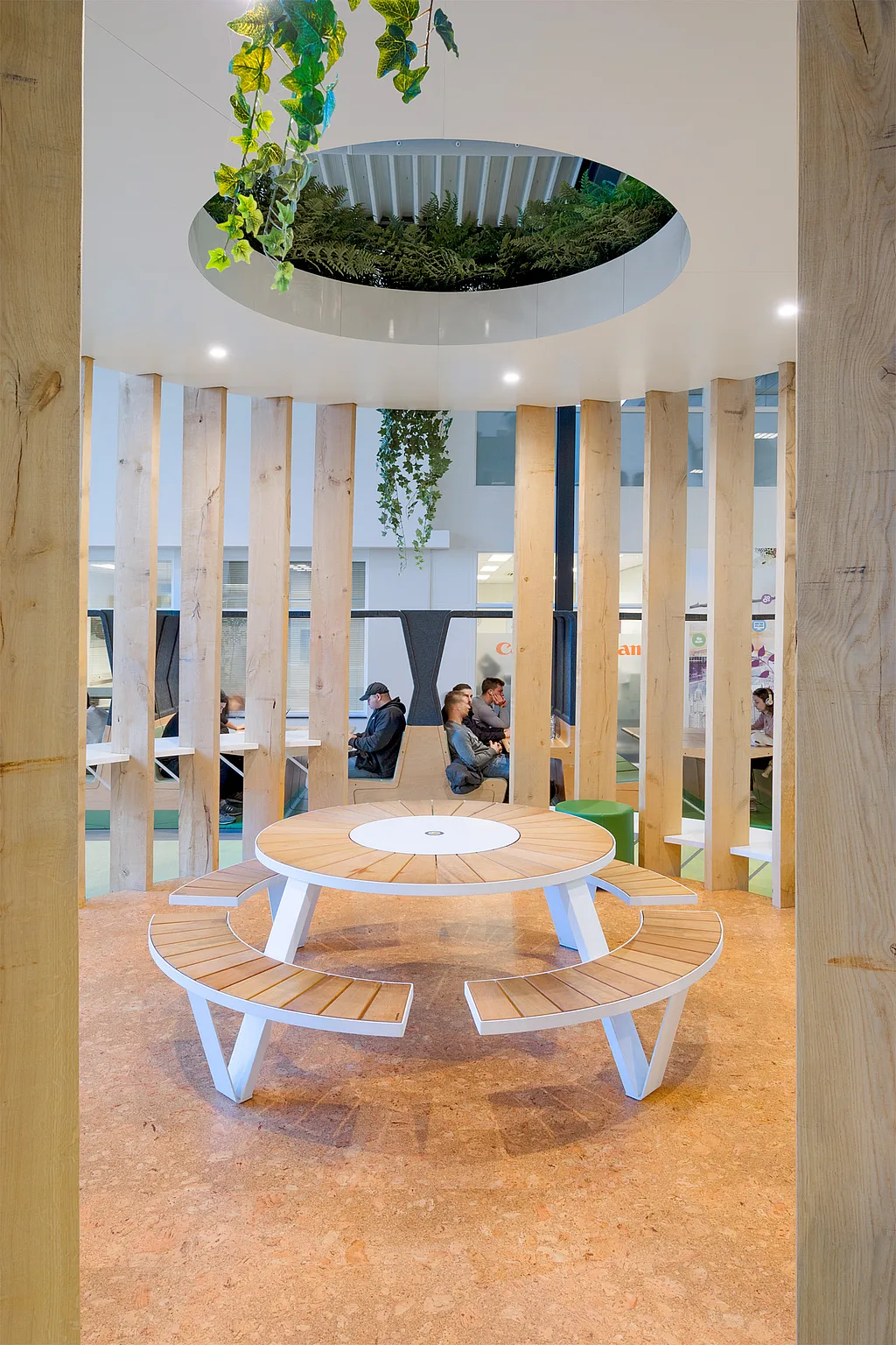 A large wooden cylinder in the middle of the hall, topped with a lush green roof, creating a striking focal point in the space.