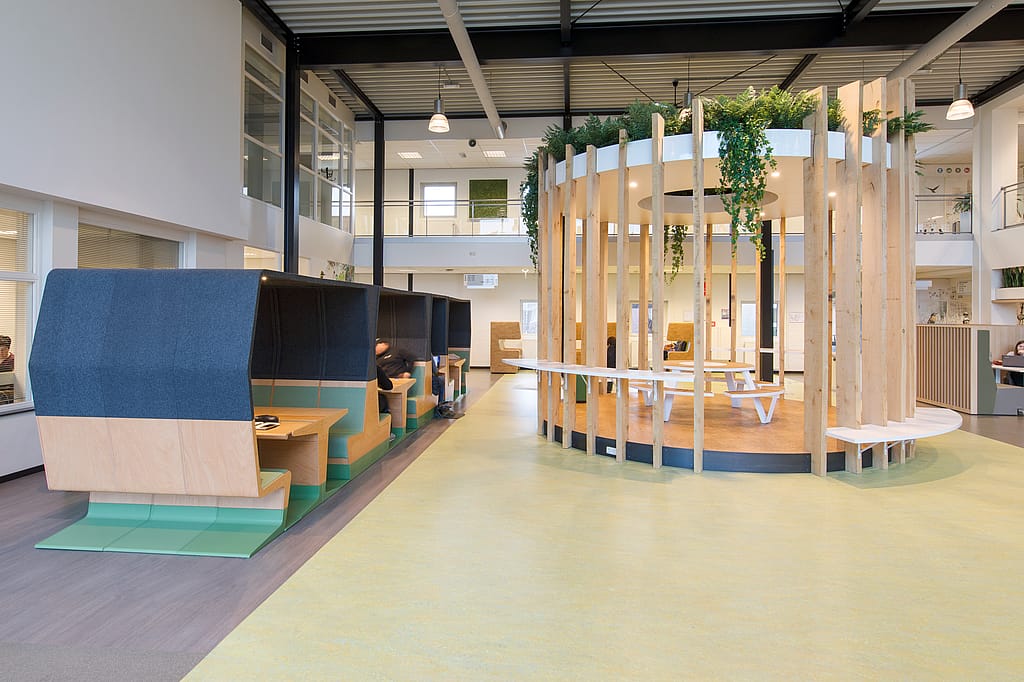Vue d'ensemble du hall d'entrée de Fontys Venlo, conçu comme une place de village couverte, avec des espaces de détente et d'étude/réunion qui invitent étudiants et personnel à s'attarder.