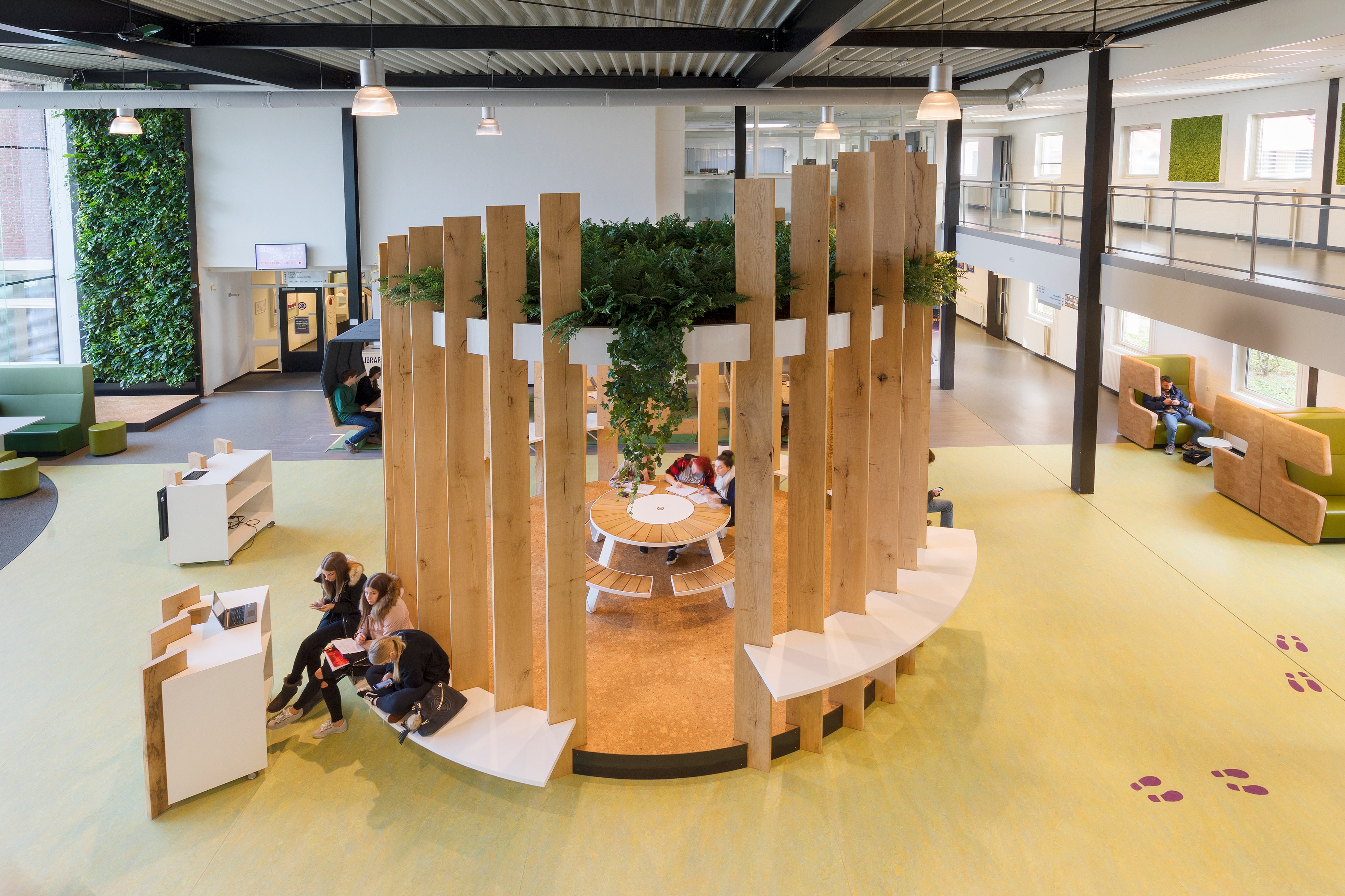 Vue d'ensemble du hall d'entrée de Fontys Venlo, conçu comme une place de village couverte, avec des espaces de détente et d'étude/réunion qui invitent étudiants et personnel à s'attarder.