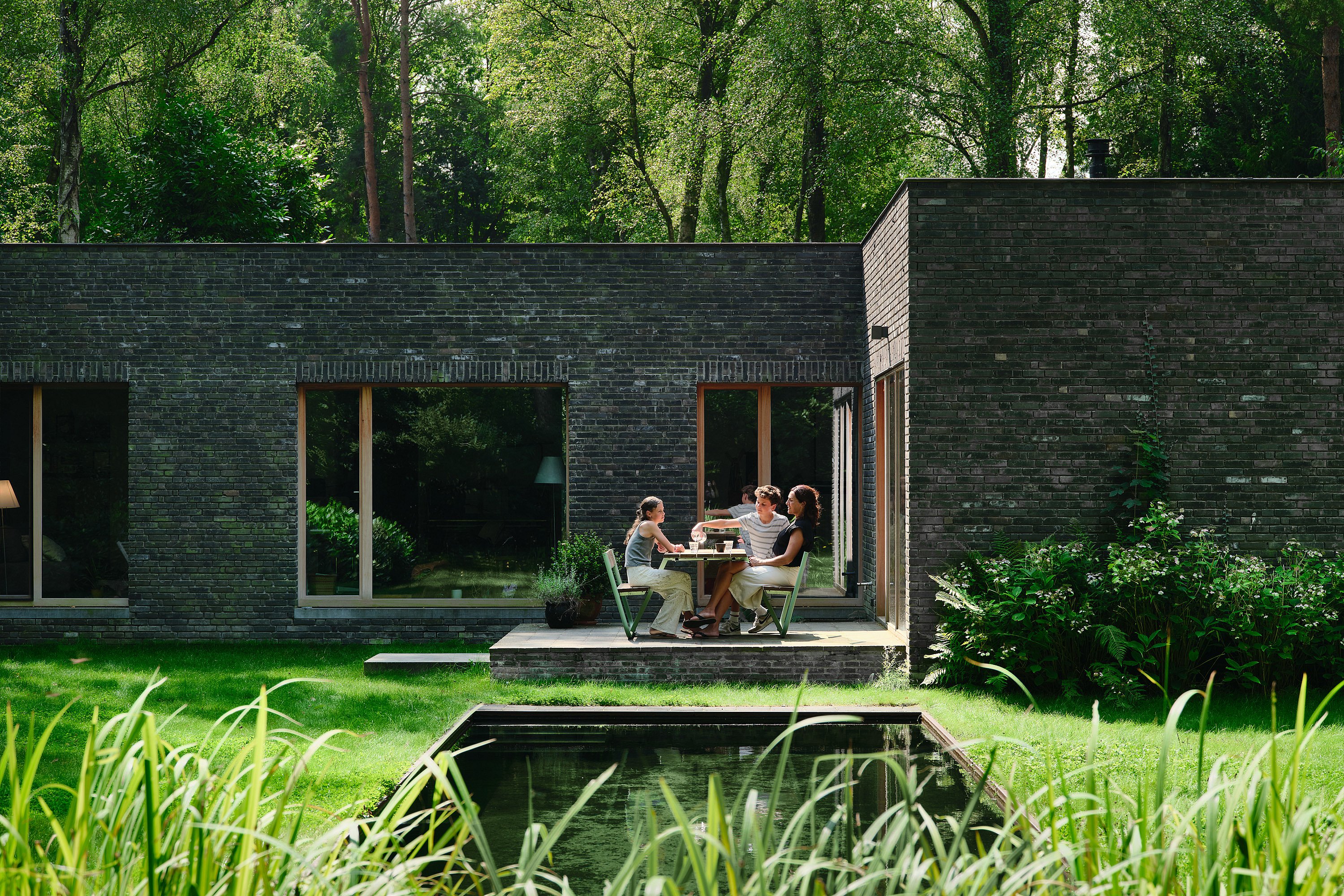 La douce finition vert pistache de la table de pique-nique Manille et des plateaux en bois de ses bancs contraste avec le feuillage du jardin, créant une ambiance calme et harmonieuse.