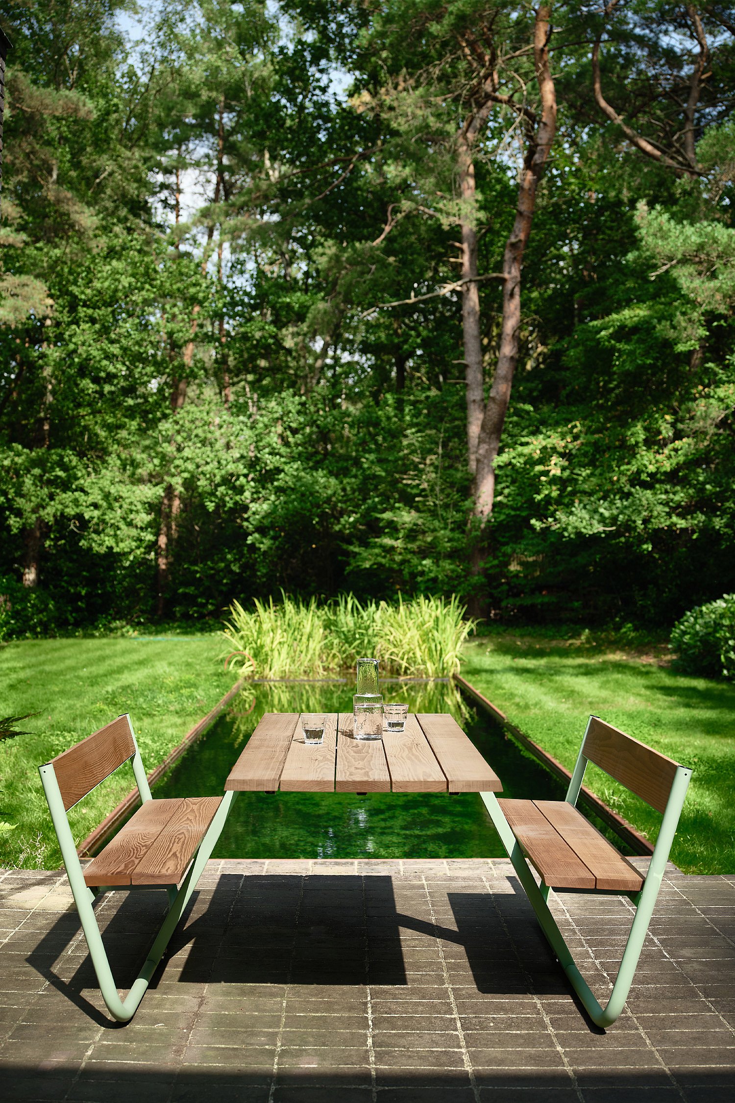 Autre angle de vue de la scène extérieure montrant l'emplacement de la table de pique-nique dans le jardin, encadrée par les arbres et la végétation pour une atmosphère de détente en plein air.