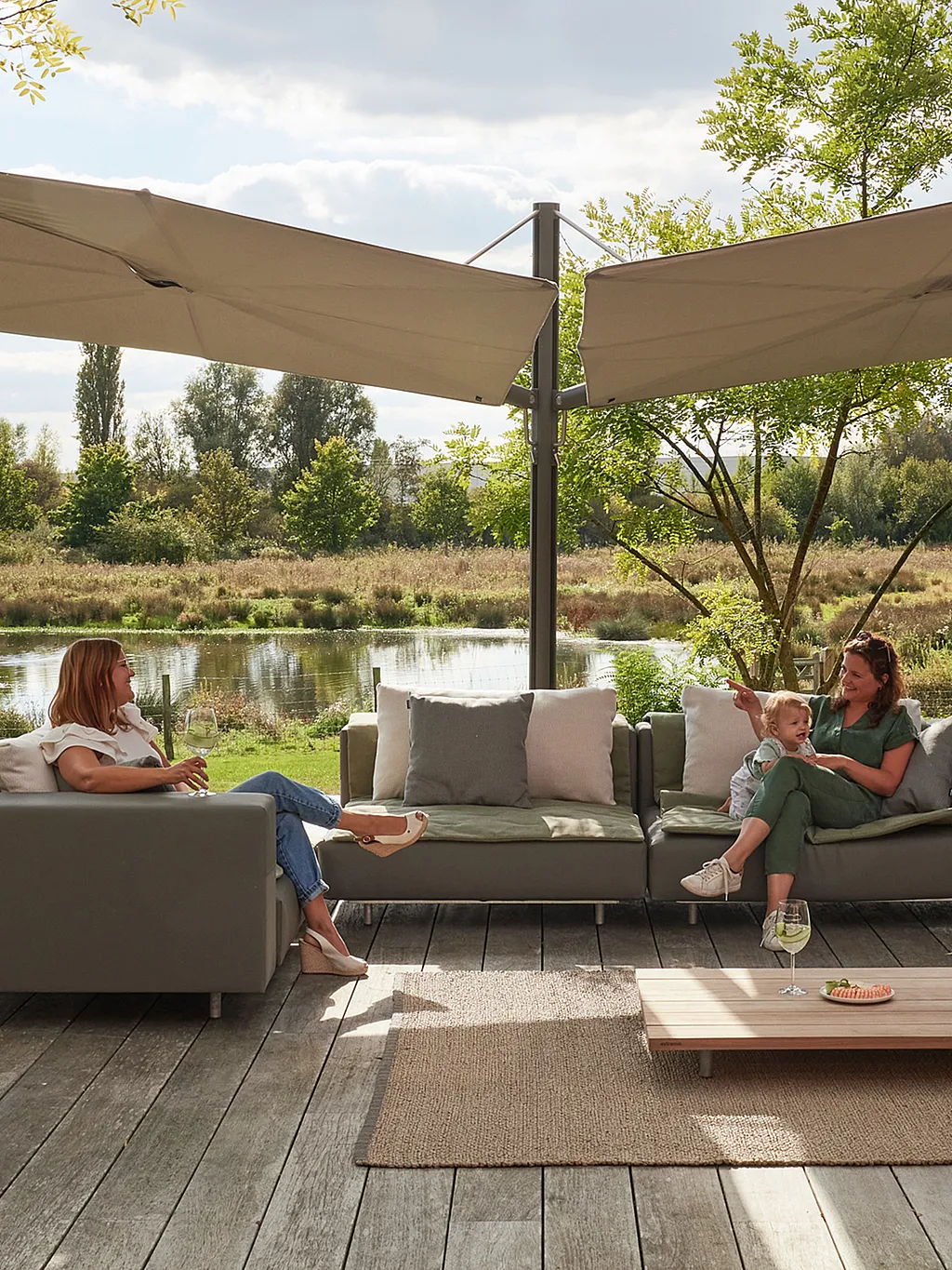Terrasse extérieure avec un salon de jardin en forme de morse et deux grands parasols Sensu Duo Diamond fixés sur un mât central unique. Chaque toile est inclinée différemment pour créer une zone d'ombre superposée.