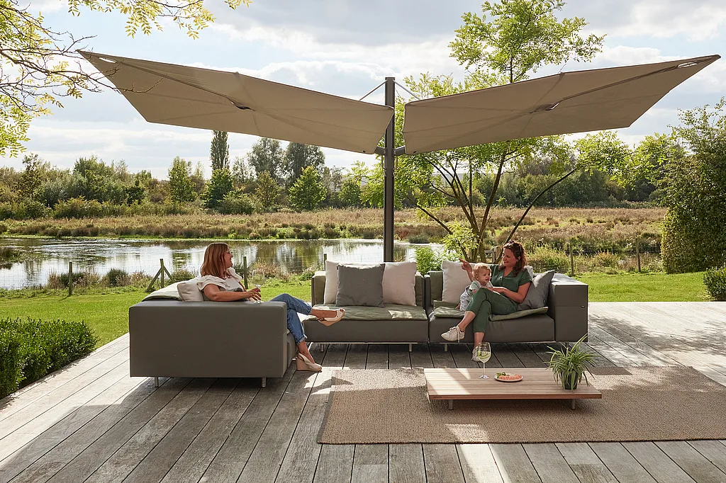 Buitenterras met de Walrus loungebank en twee grote Sensu Duo Diamond parasols gemonteerd op één centrale paal, waarbij elk doek in een andere hoek is geplaatst om overlappende schaduw te creëren.