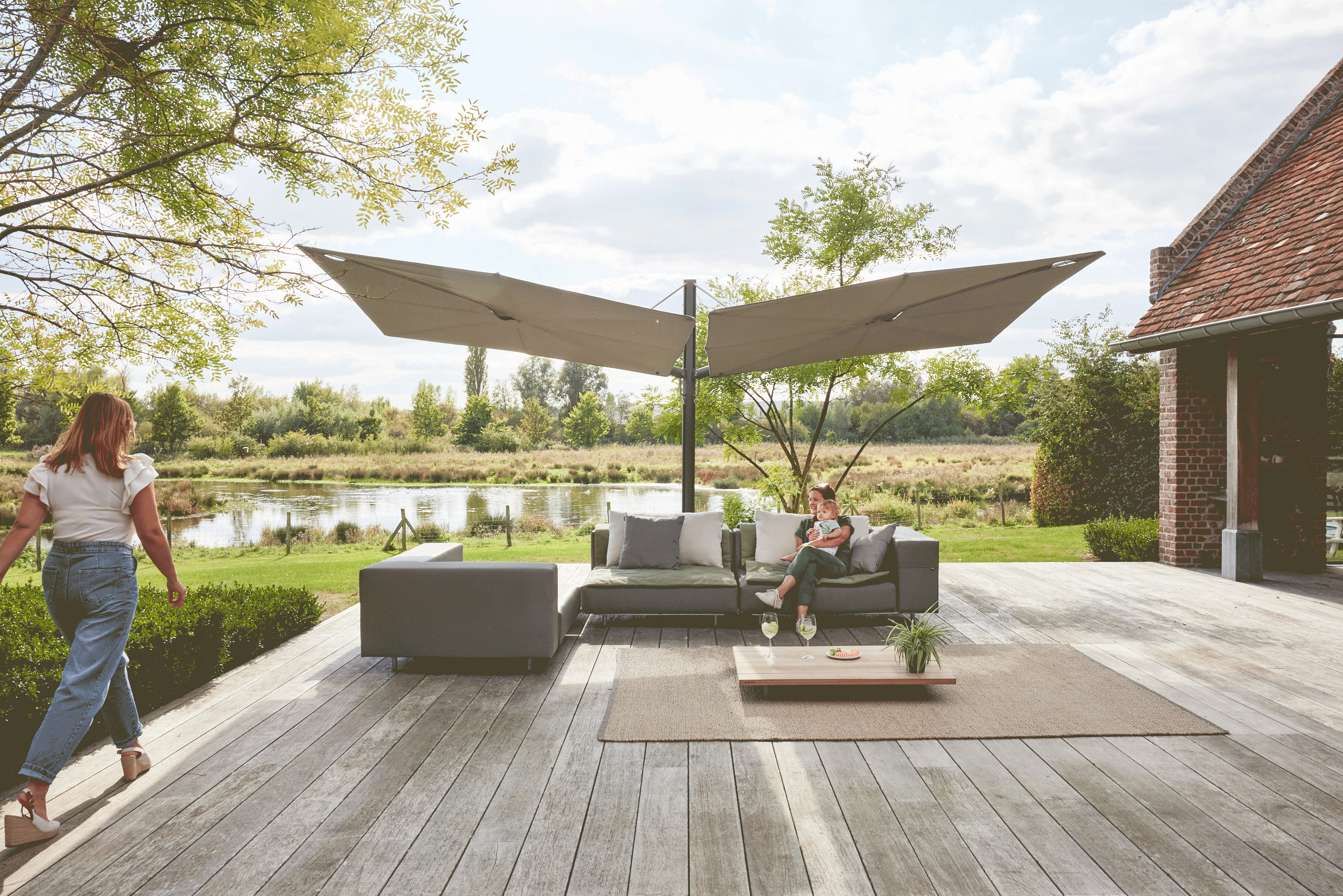   Weitblick auf die Terrasse mit modularen Loungemöbeln unter zwei Sonnenschirmen, umgeben von gepflegten Grünflächen.