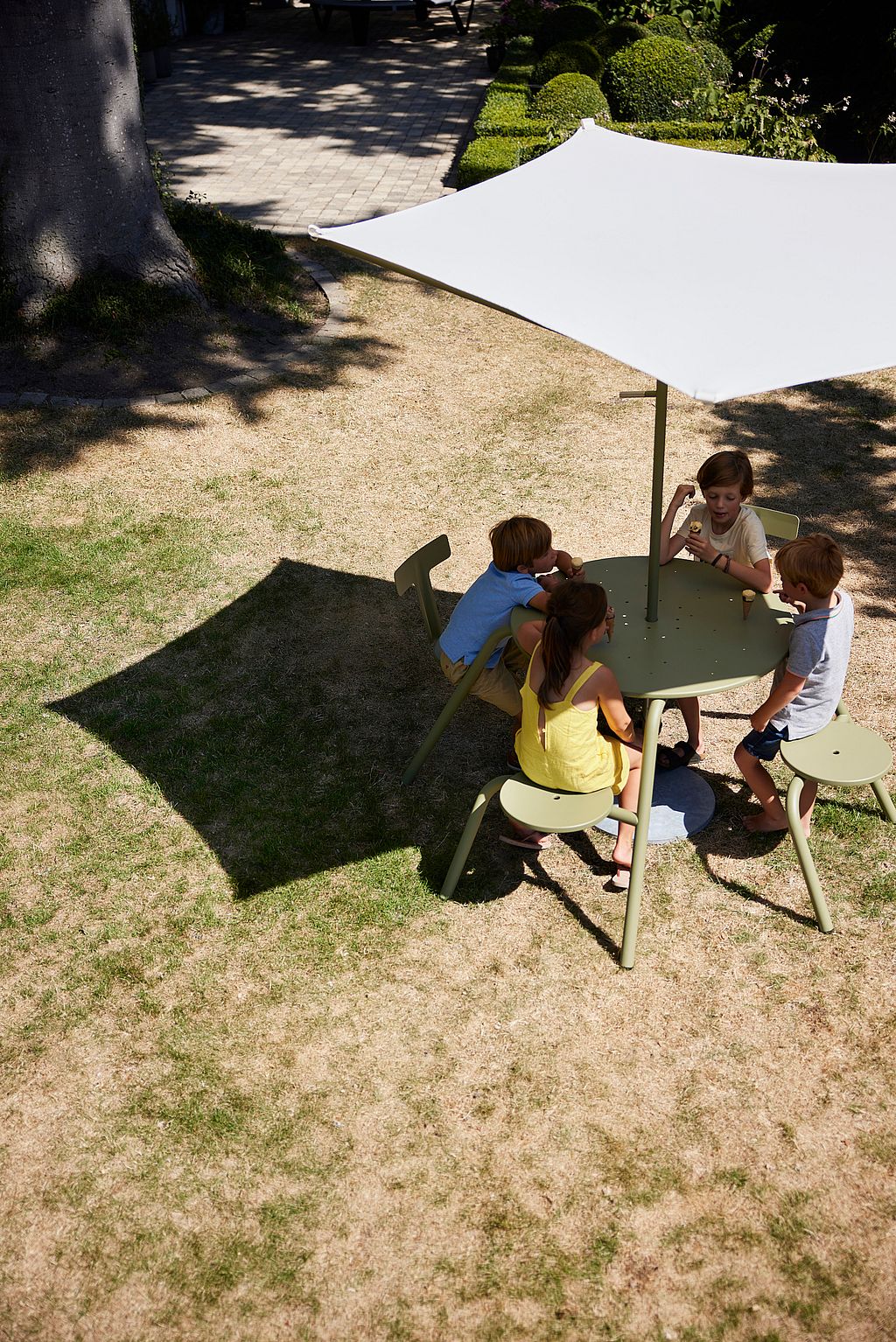 Overzicht van een Virus picknicktafel met geïntegreerde banken in een groene omgeving. Vier mensen zitten aan de tafel te midden van tuinplanten.