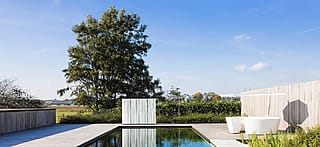Ein großzügiger Außenbereich mit dem Kosmos-Tisch und den STICKS-Elementen auf einer hellen Terrasse neben einem modernen Swimmingpool.