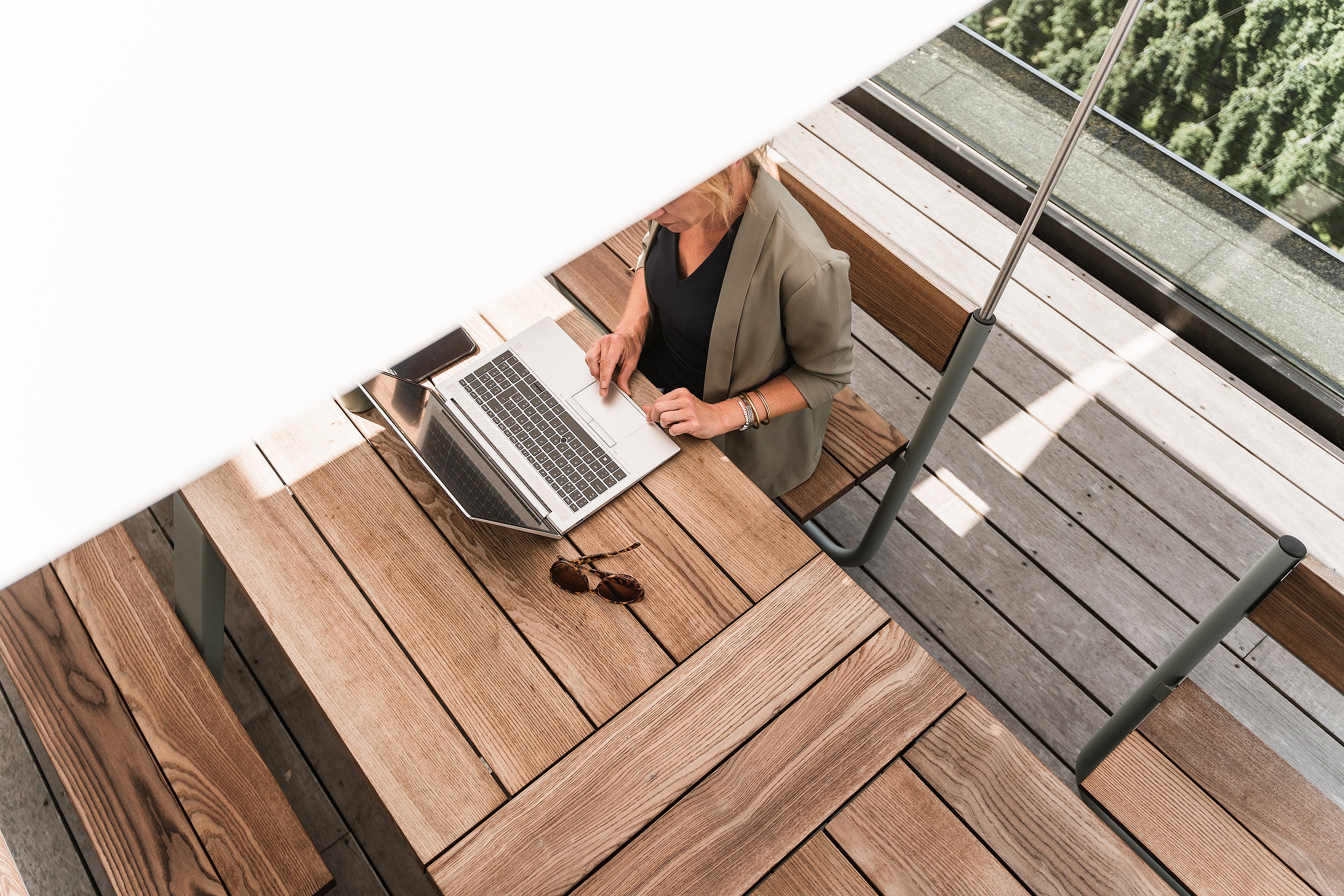 Top view of a woman working on a laptop at a wooden Manille table, partly shaded by the white canopy above.