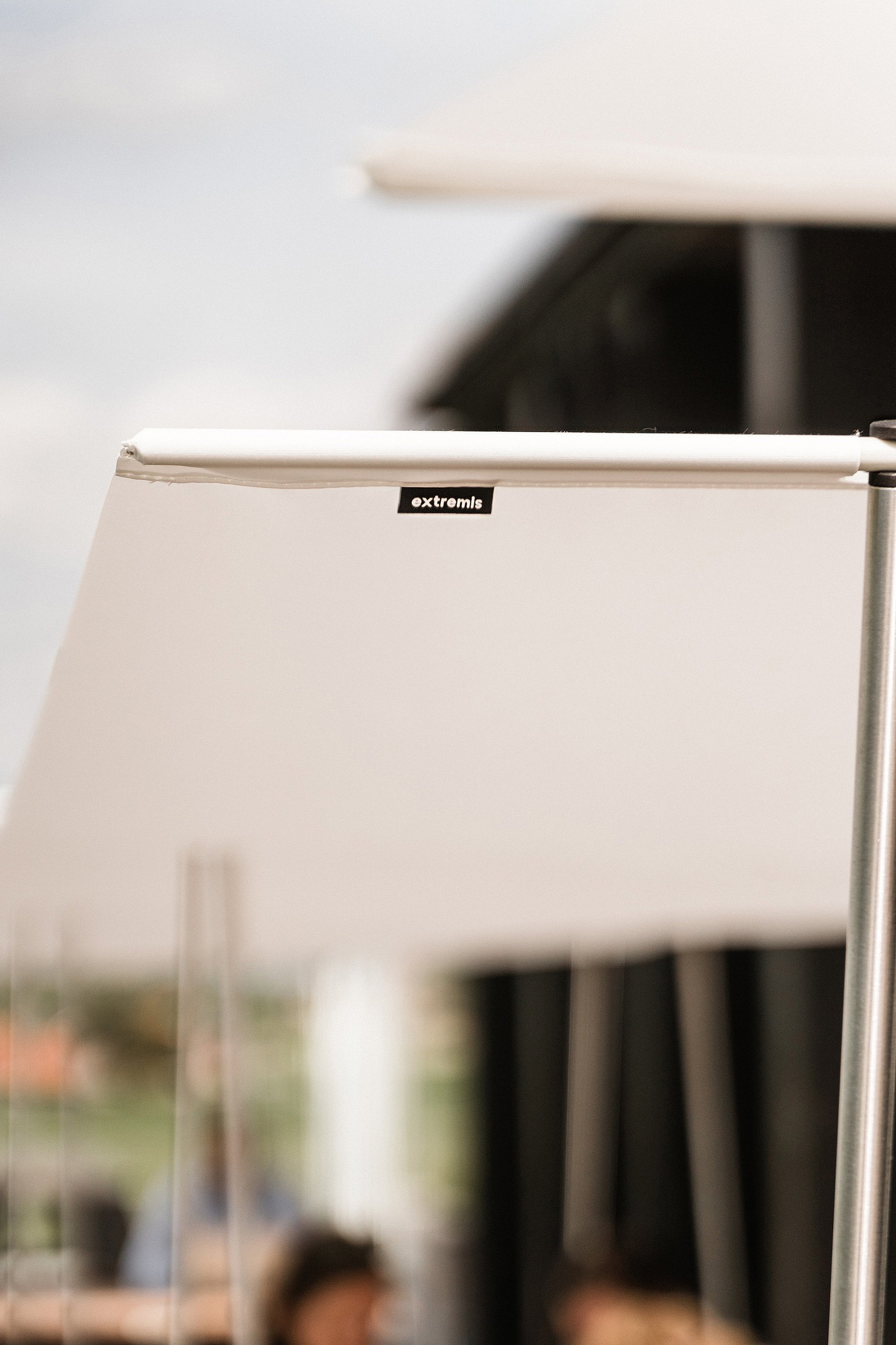 Close-up of the white Manille shade fabric and pole, with the Extremis label visible and the terrace softly blurred behind.