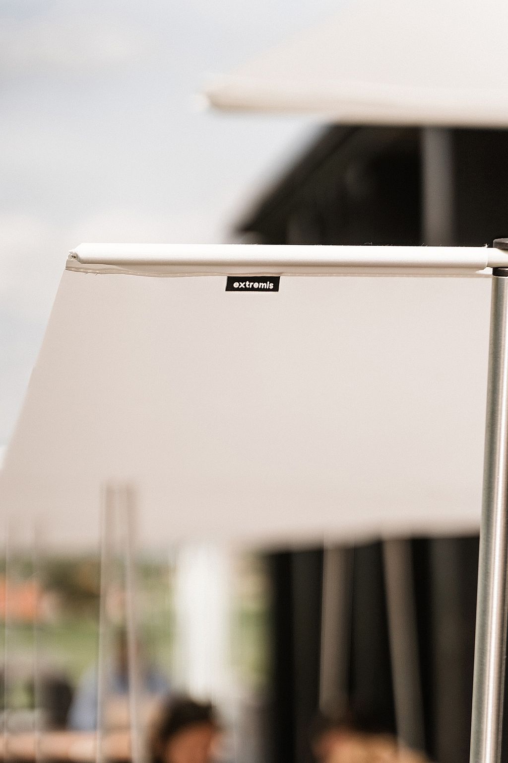 Close-up of the white Manille shade fabric and pole, with the Extremis label visible and the terrace softly blurred behind.