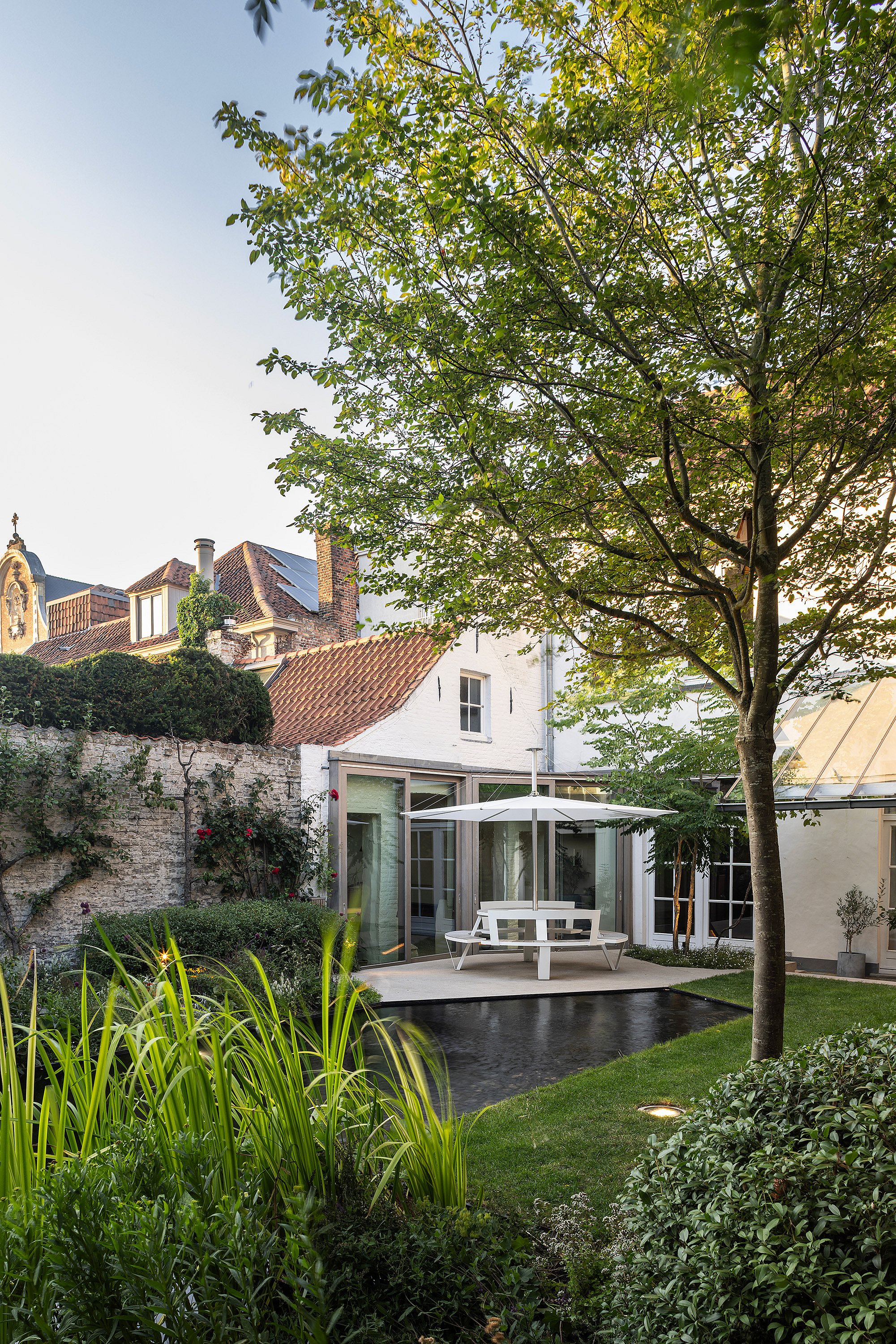 Weitwinkelaufnahme der Hausfassade und des Glasdachs, wobei der Teich die Innen- und Gartenbeleuchtung reflektiert.