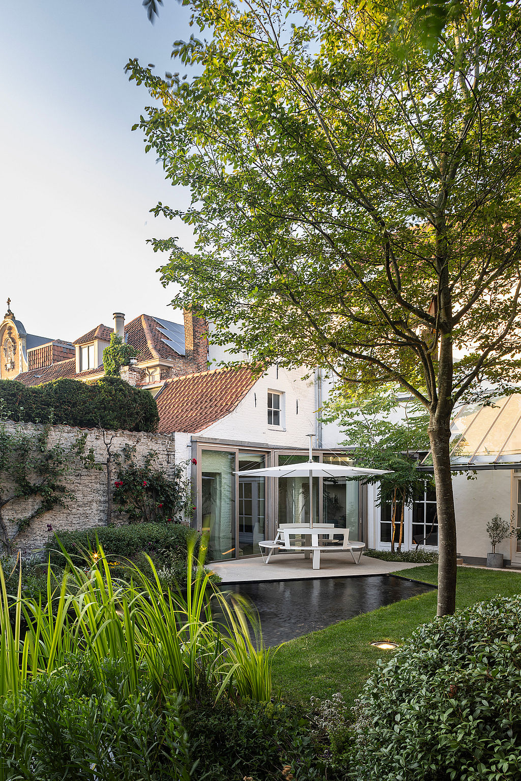 Weitwinkelaufnahme der Hausfassade und des Glasdachs, wobei der Teich die Innen- und Gartenbeleuchtung reflektiert.
