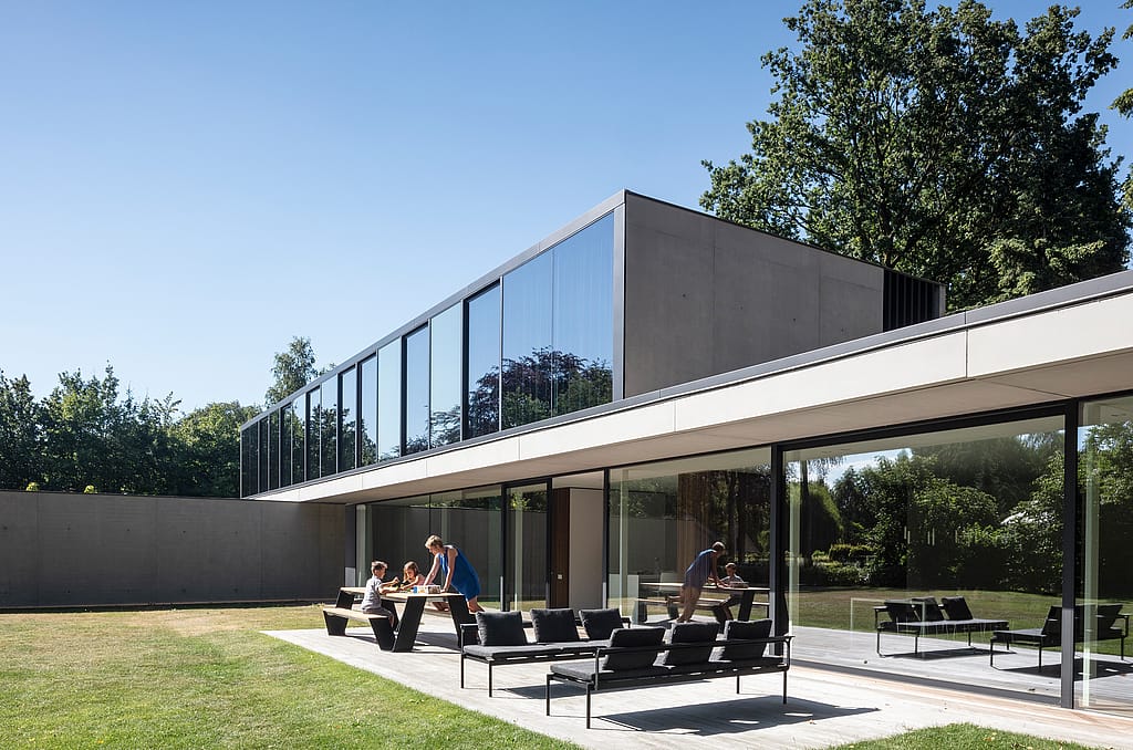 Vaste terrasse de plain-pied avec un salon de jardin modulable foncé, disposé sur de grandes dalles claires, donnant sur des champs verdoyants sous un ciel bleu azur.