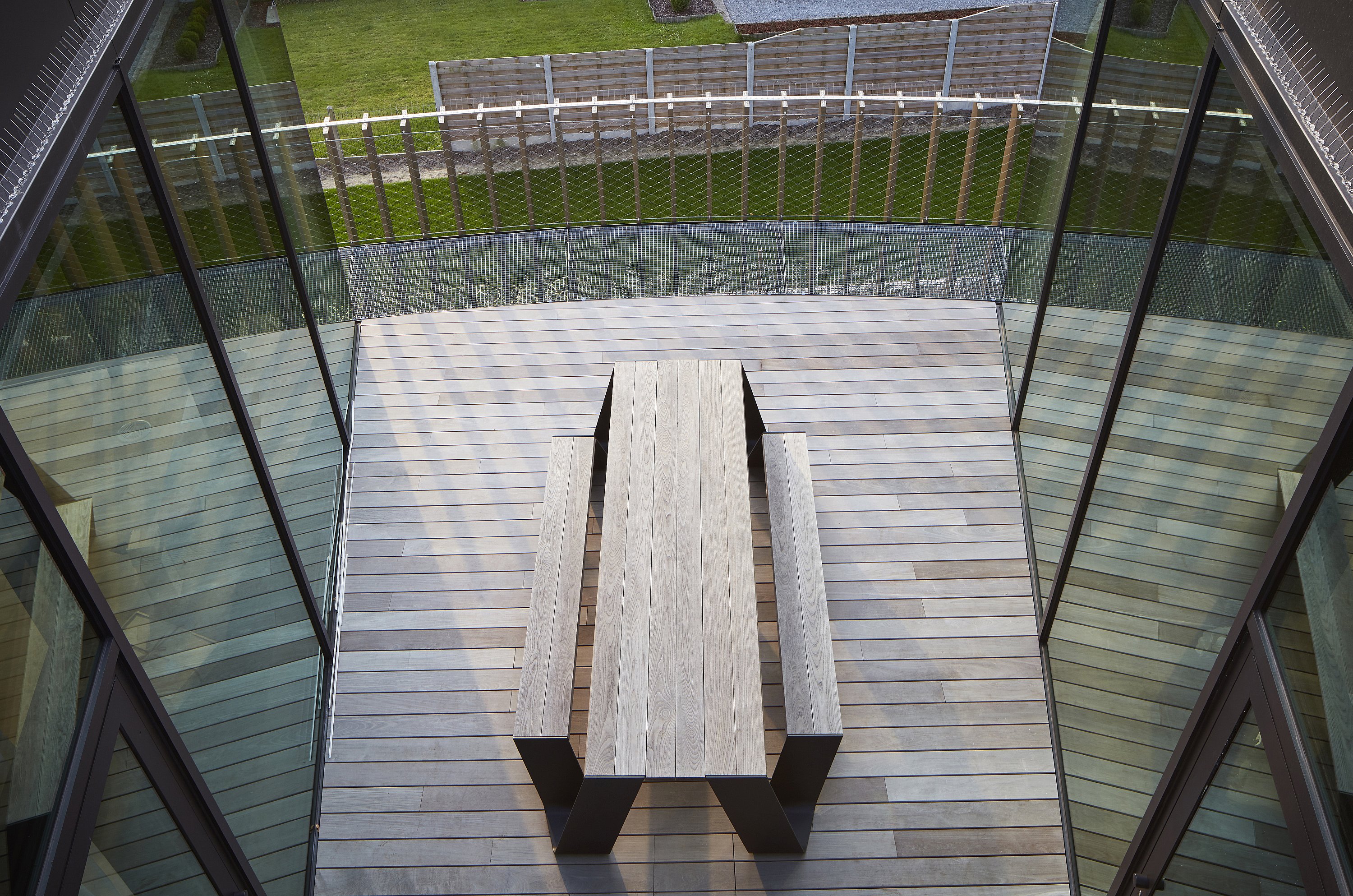 Bovenaanzicht van een compacte patio met een verweerde houten hoptafel tussen hoge glazen wanden.