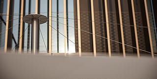 Close-up van de centrale mast en spankabels van een Inumbra parasol tegen de gestreepte gevel van het kantoorgebouw