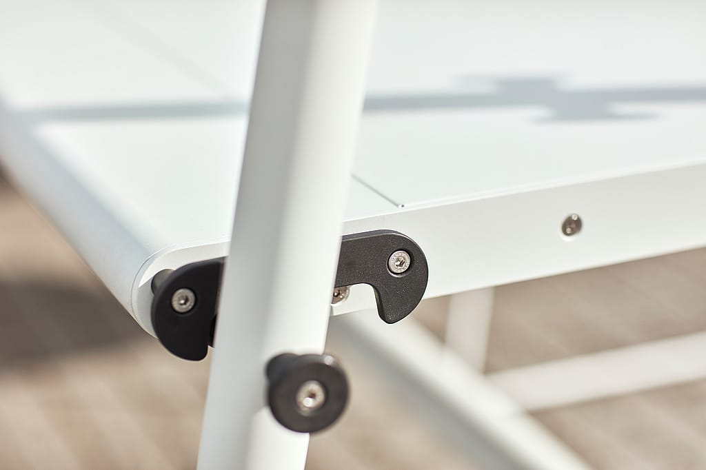 Close up of a black hinge bracket and bolts on the white Tiki table frame.