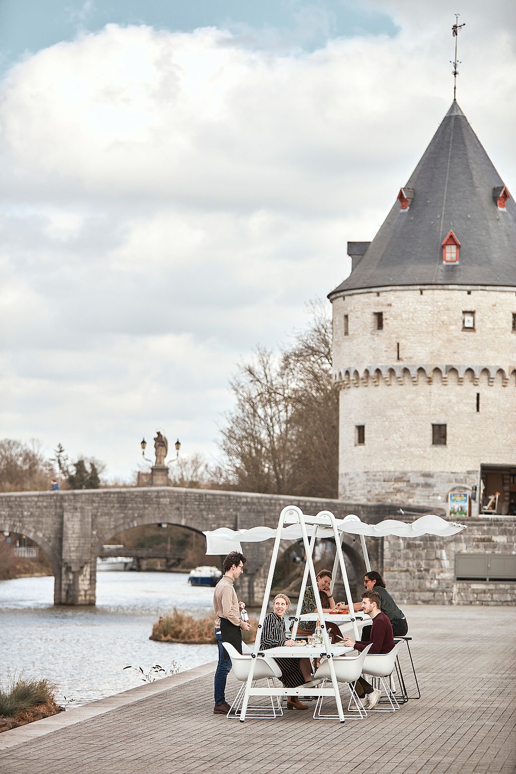 Group of people dining at the Tiki table with a tower and stone bridge in the background.