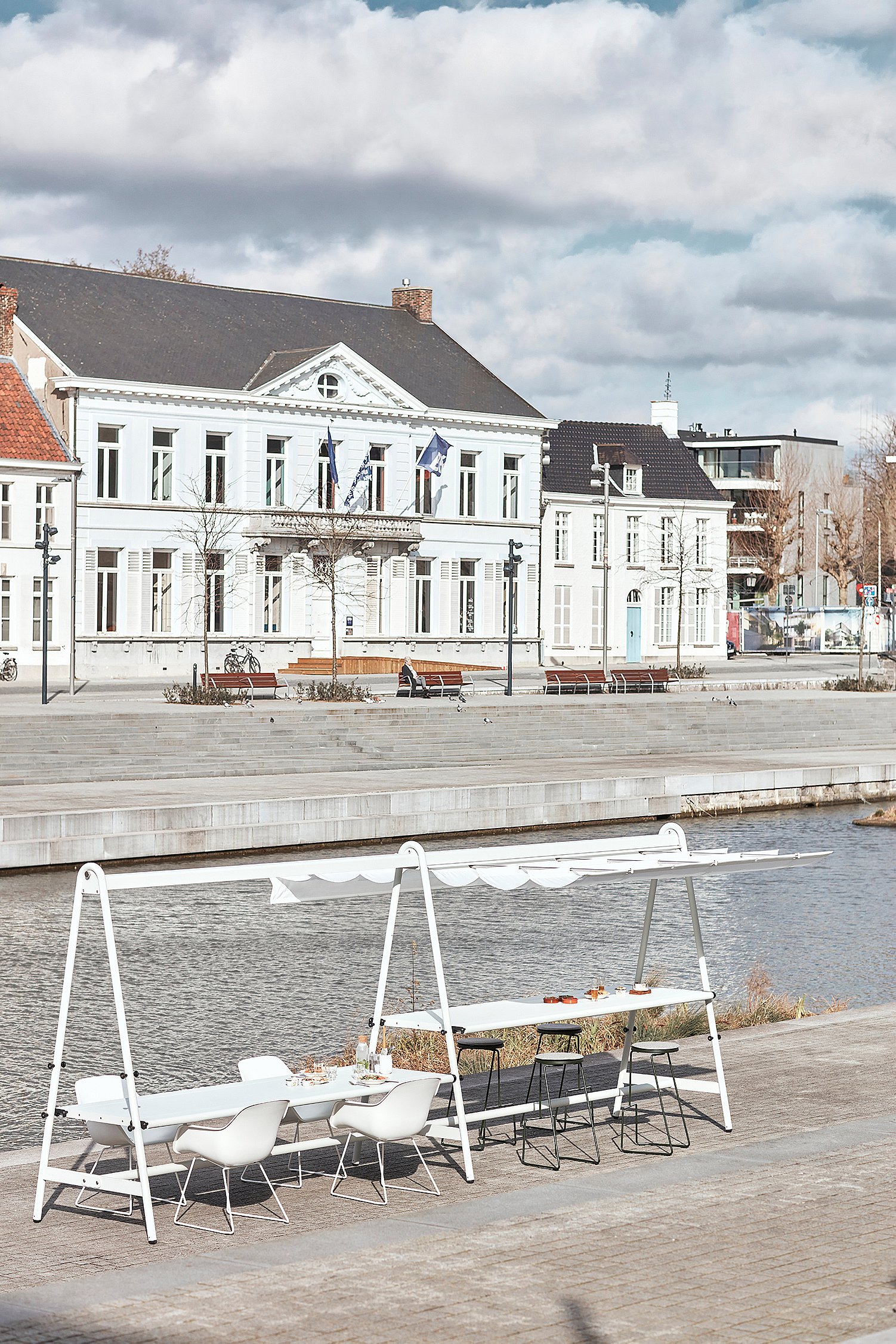 Empty Tiki table and stools set along the river with historic buildings across the water.