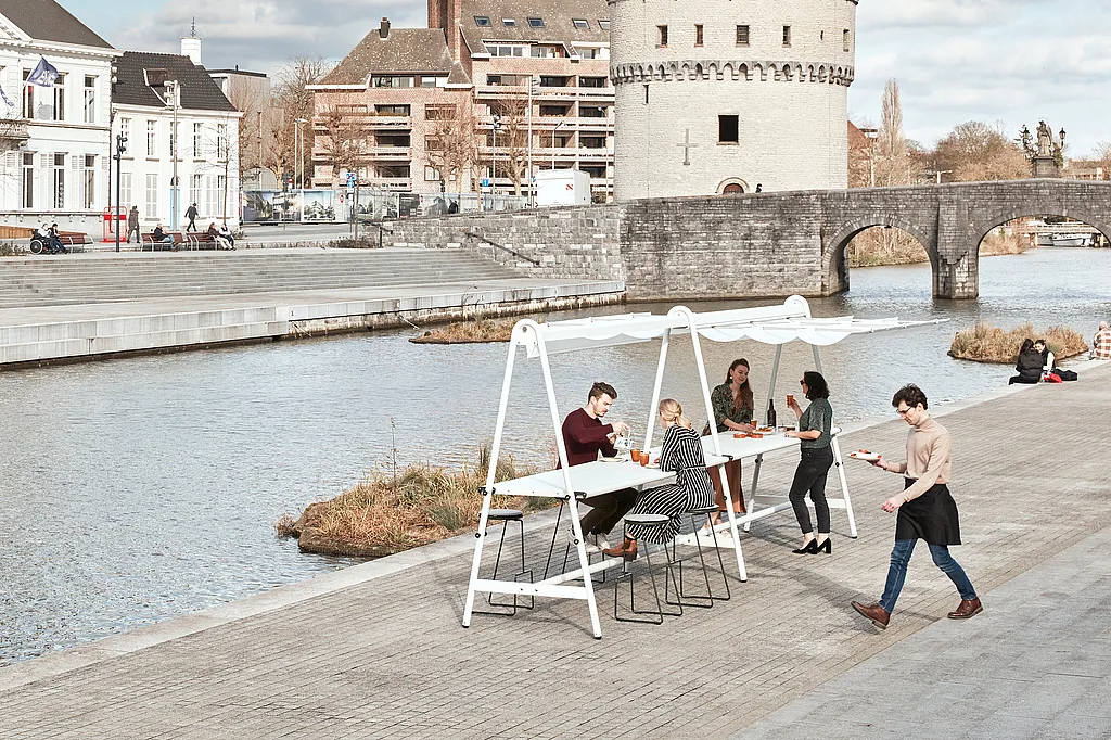Vertical view of the outdoor dining setup on the riverside, with the Broel Tower behind and a server passing in front.
