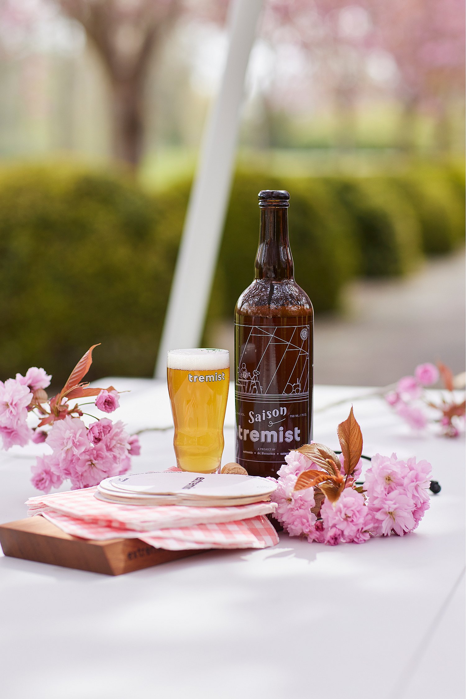 Eine Tremist-Flasche und ein Glas Bier stehen auf einem weißen Tisch neben rosa Kirschblüten.