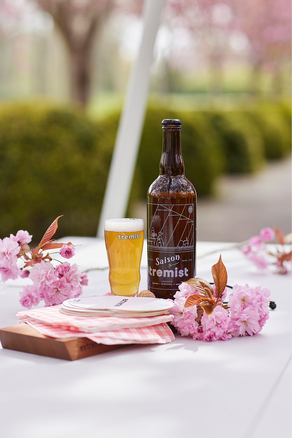Eine Tremist-Flasche und ein Glas Bier stehen auf einem weißen Tisch neben rosa Kirschblüten.