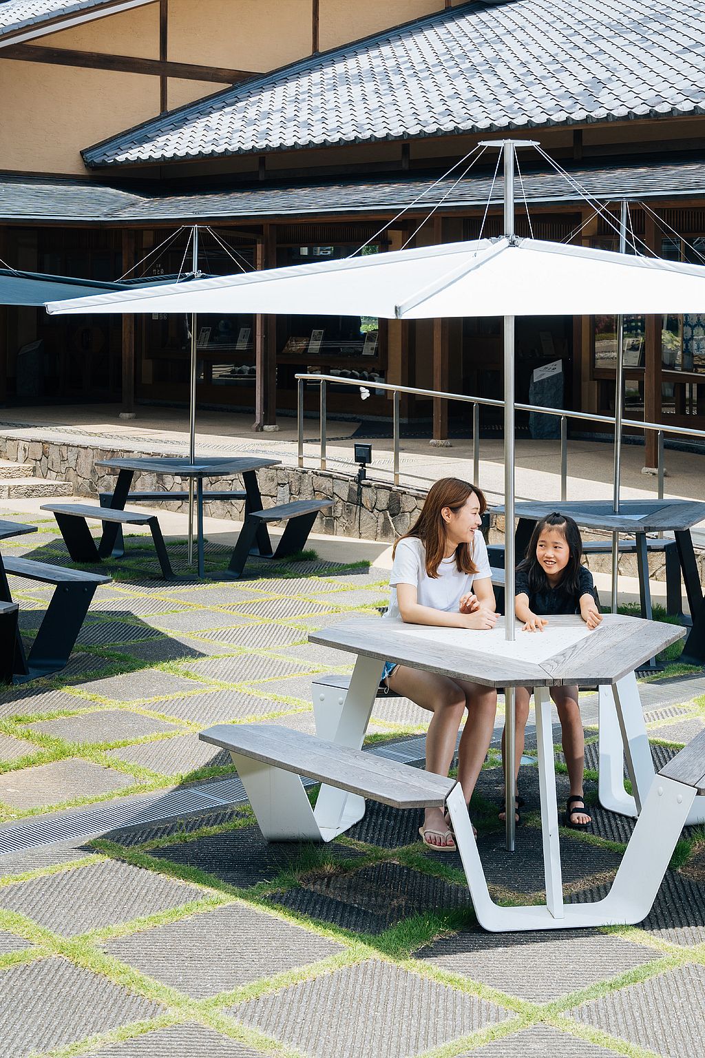Eine Frau und ein Kind sitzen auf den Anker-Sitzmöbeln mit Sonnenschirm im Kunsthandwerkszentrum in Japan