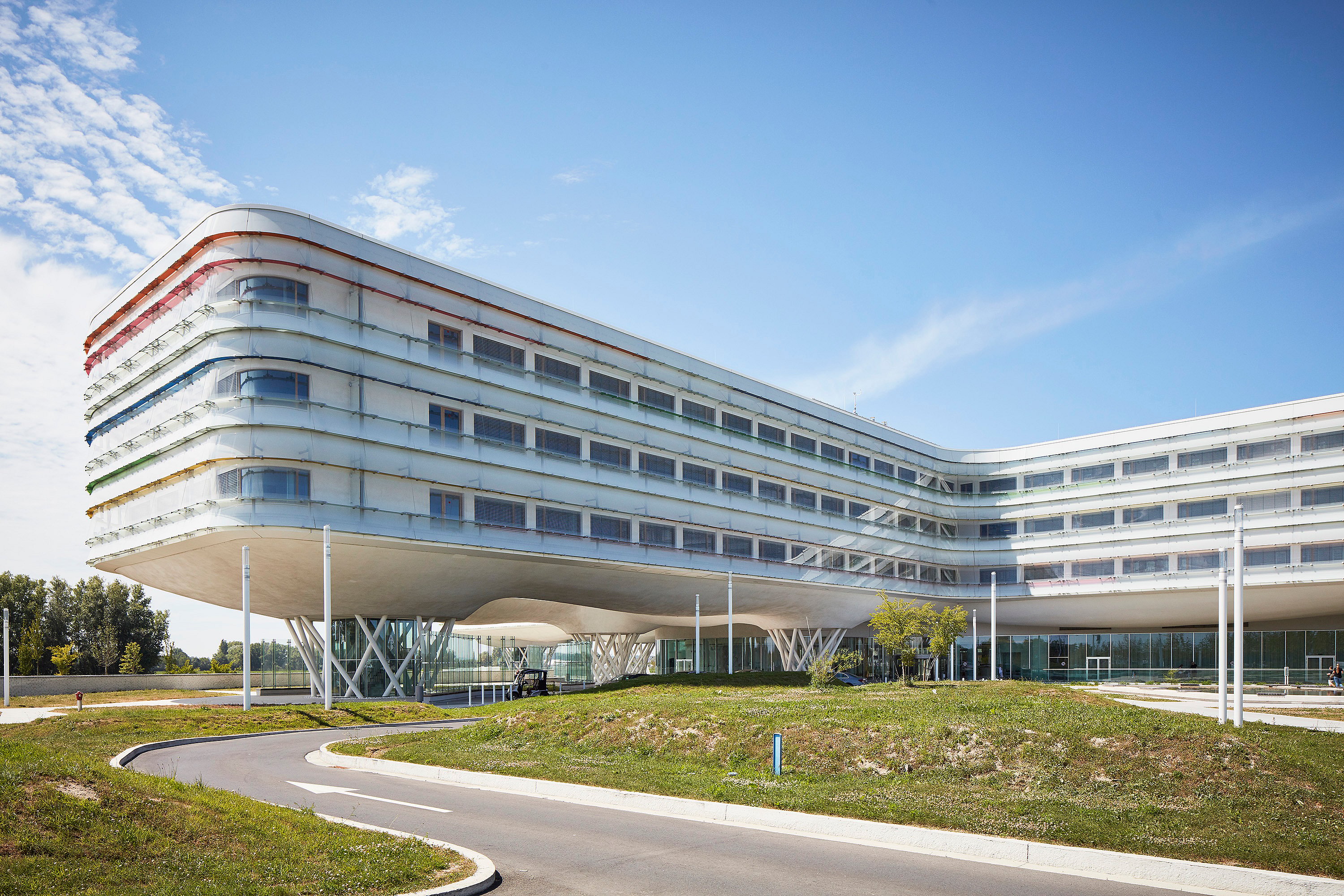   Weitwinkelaufnahme des Klinikgeländes, die das moderne Design des Krankenhauses, die Sitzbereiche im Freien und die landschaftlich gestaltete Umgebung zeigt.