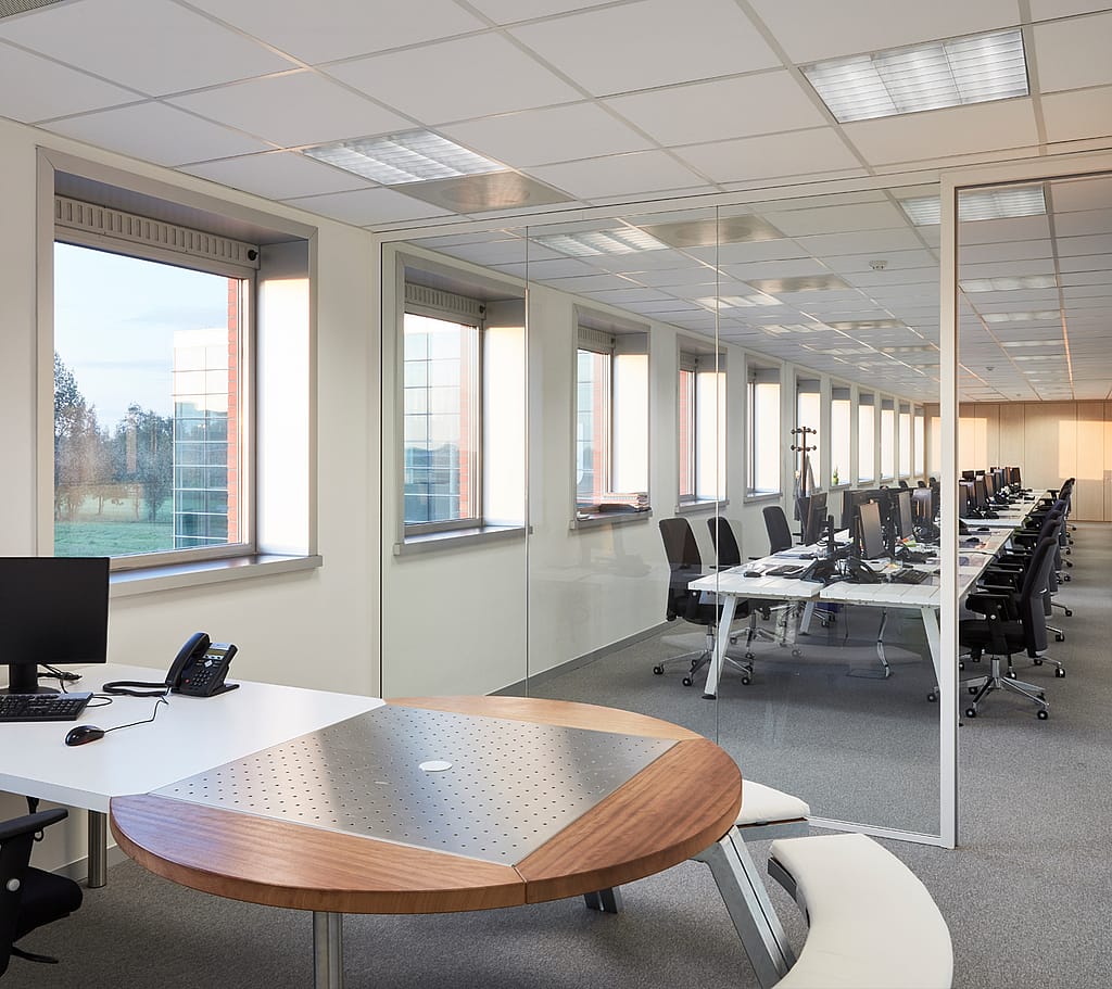 Interieurfoto van de CCV-kantoren met een mix van banken en stoelen rond houten tafels; waar medewerkers kunnen samenwerken en apparaten gebruiken in een lichte, open kantooromgeving.