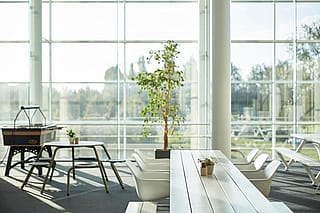 Een breed interieurbeeld van de eetruimte van CCV Offices, met zitplaatsen aan lange Marina-tafels en -banken; grote ramen en moderne kantoorverlichting creëren een lichte, collaboratieve omgeving.
