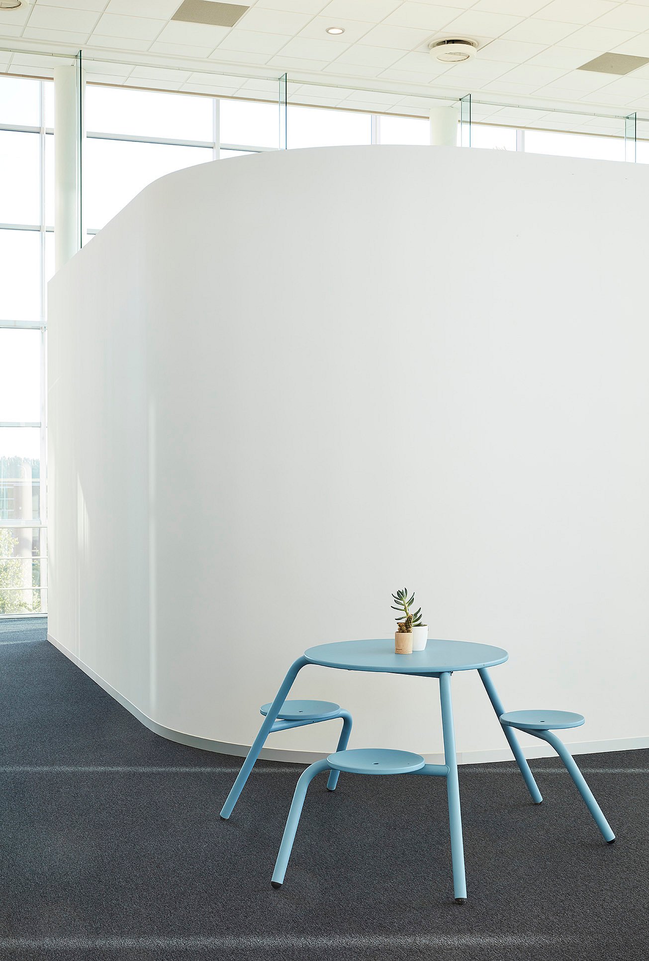 Een kantoorinterieur met een gebogen witte wand, met een lichtblauwe Virus-tafel met geïntegreerde zitplaatsen.