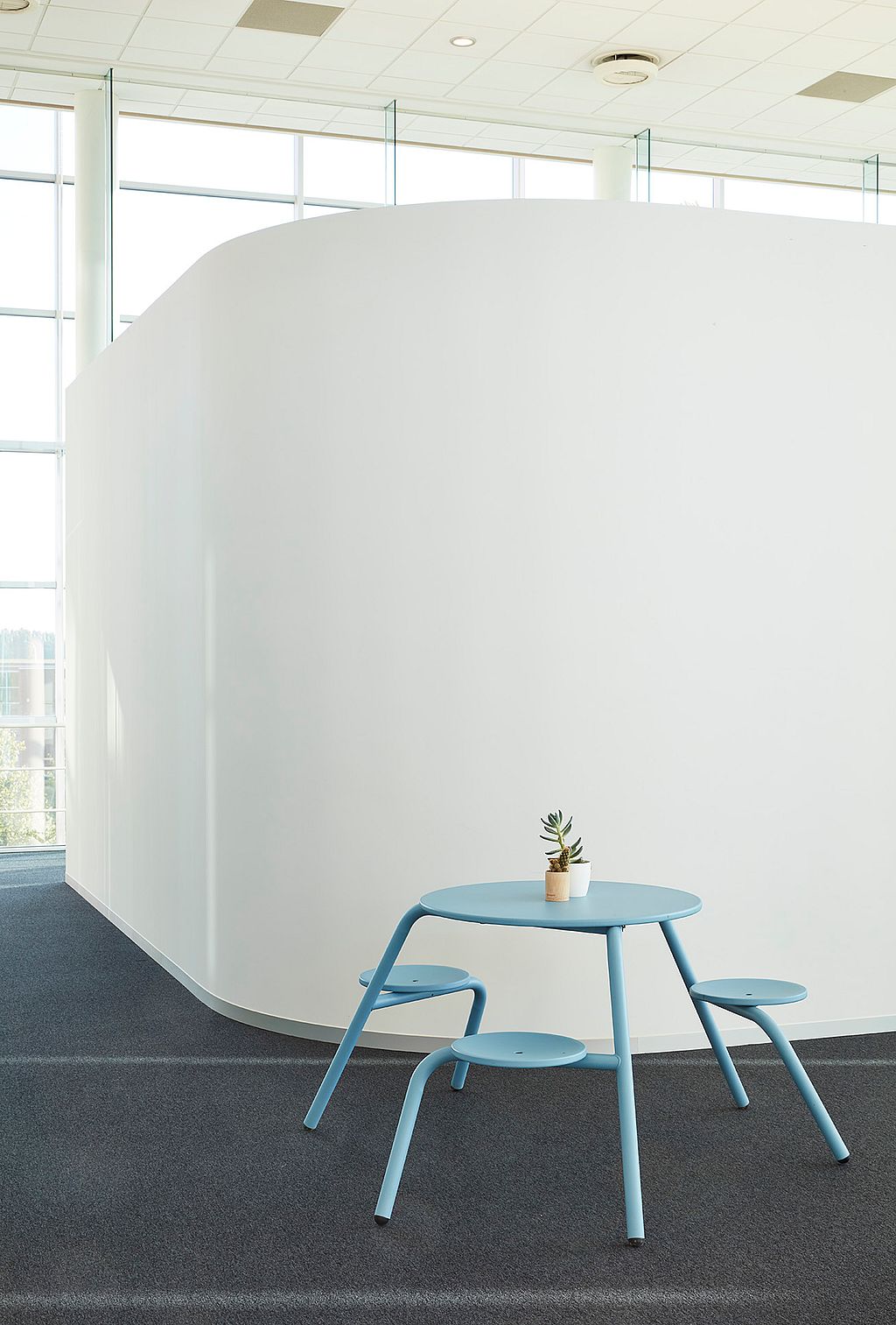 Een kantoorinterieur met een gebogen witte wand, met een lichtblauwe Virus-tafel met geïntegreerde zitplaatsen.