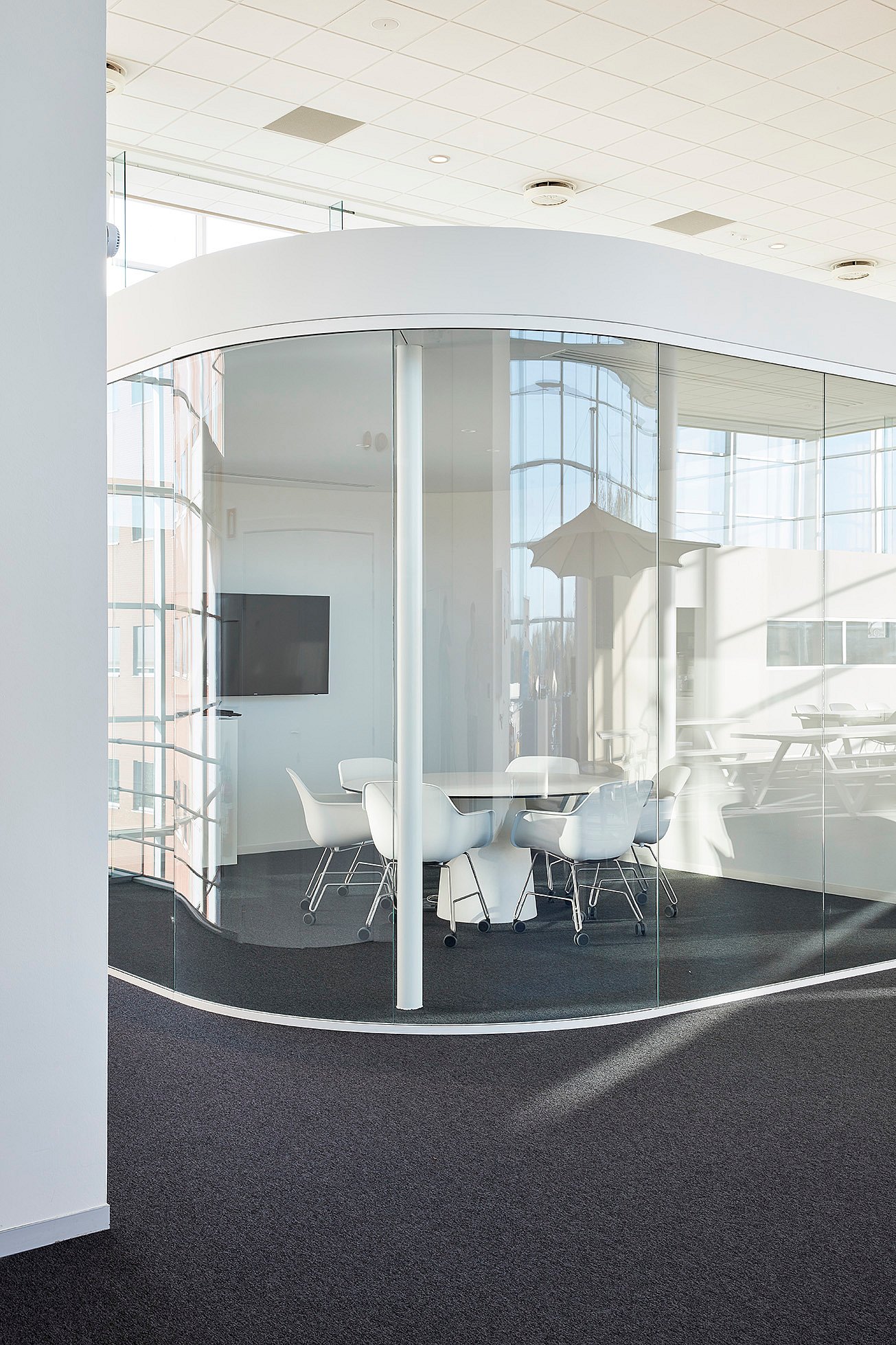 Een vergaderruimte met gebogen glas in een modern kantoor, met een ronde witte tafel omringd door witte Captain's stoelen.