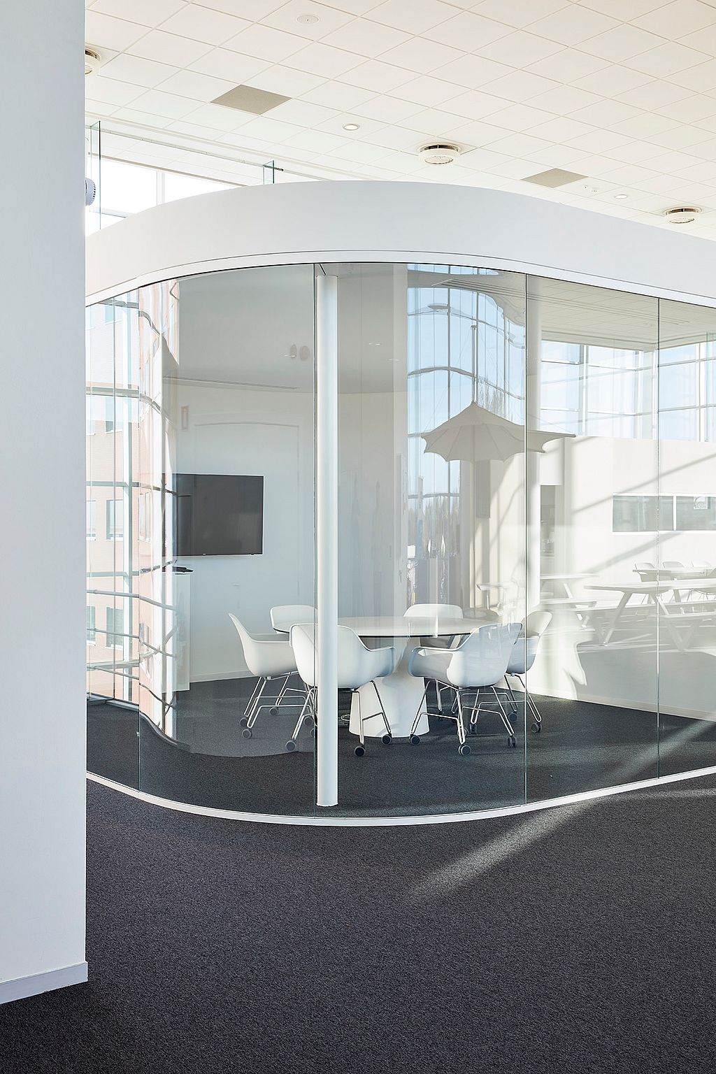 Een vergaderruimte met gebogen glas in een modern kantoor, met een ronde witte tafel omringd door witte Captain's stoelen.
