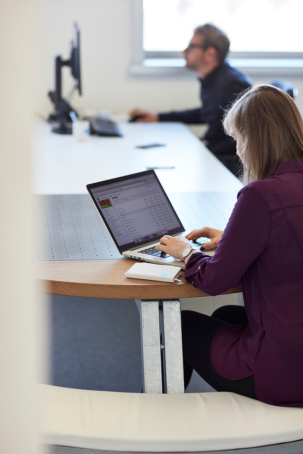 Een andere hoek van de werkruimte met gemeenschappelijke houten zit- en tafelopstellingen, waar medewerkers vergaderen en individuele taken uitvoeren.