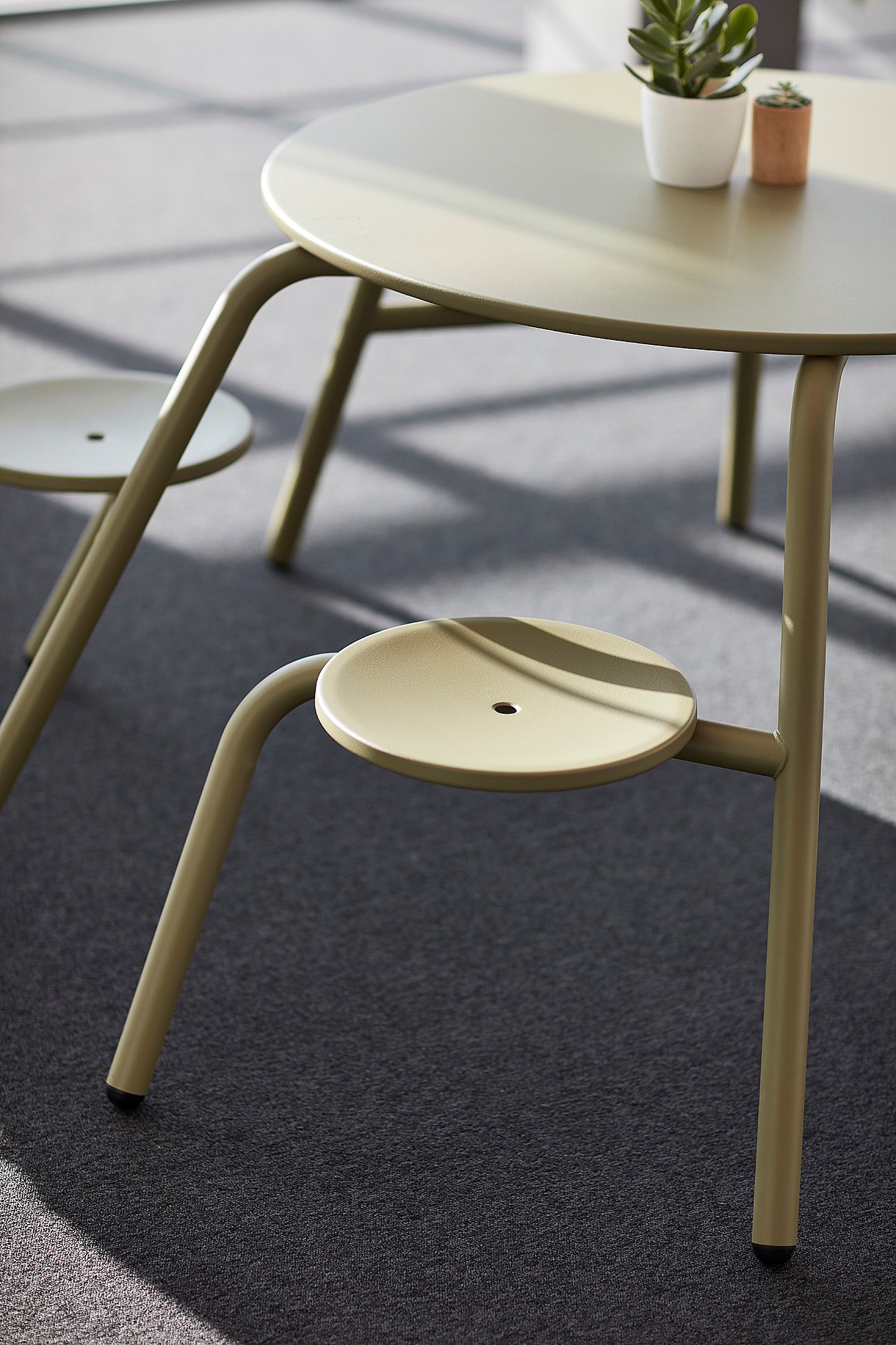 Een kantoorinterieur met een gebogen witte wand, met een groene Virus-tafel met geïntegreerde zitplaatsen en een klein potplantje in het midden.