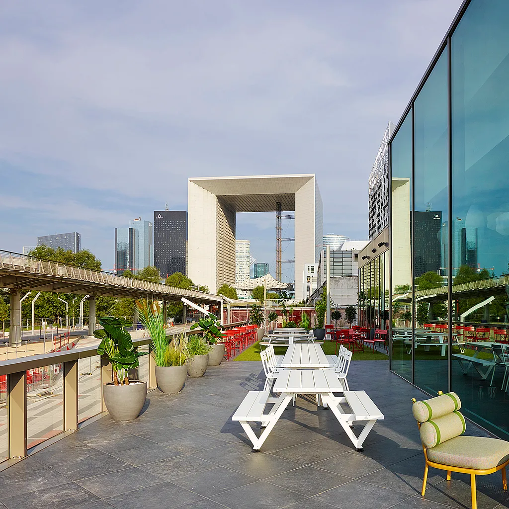 Weitläufige Außenansicht des modernen citizenM Hotel Paris in La Défense. Die komplett verglaste Fassade reflektiert das Licht und die Skyline der Stadt.