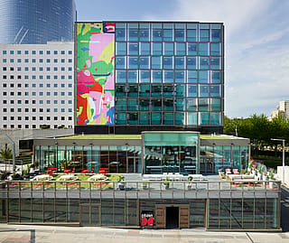 Sonnige Hotelterrasse mit rundem Pantagruel- und Marina-Tisch und Stühlen für Drinks. Blick auf die große Terrasse mit Blick auf die Grande Arche in Paris.