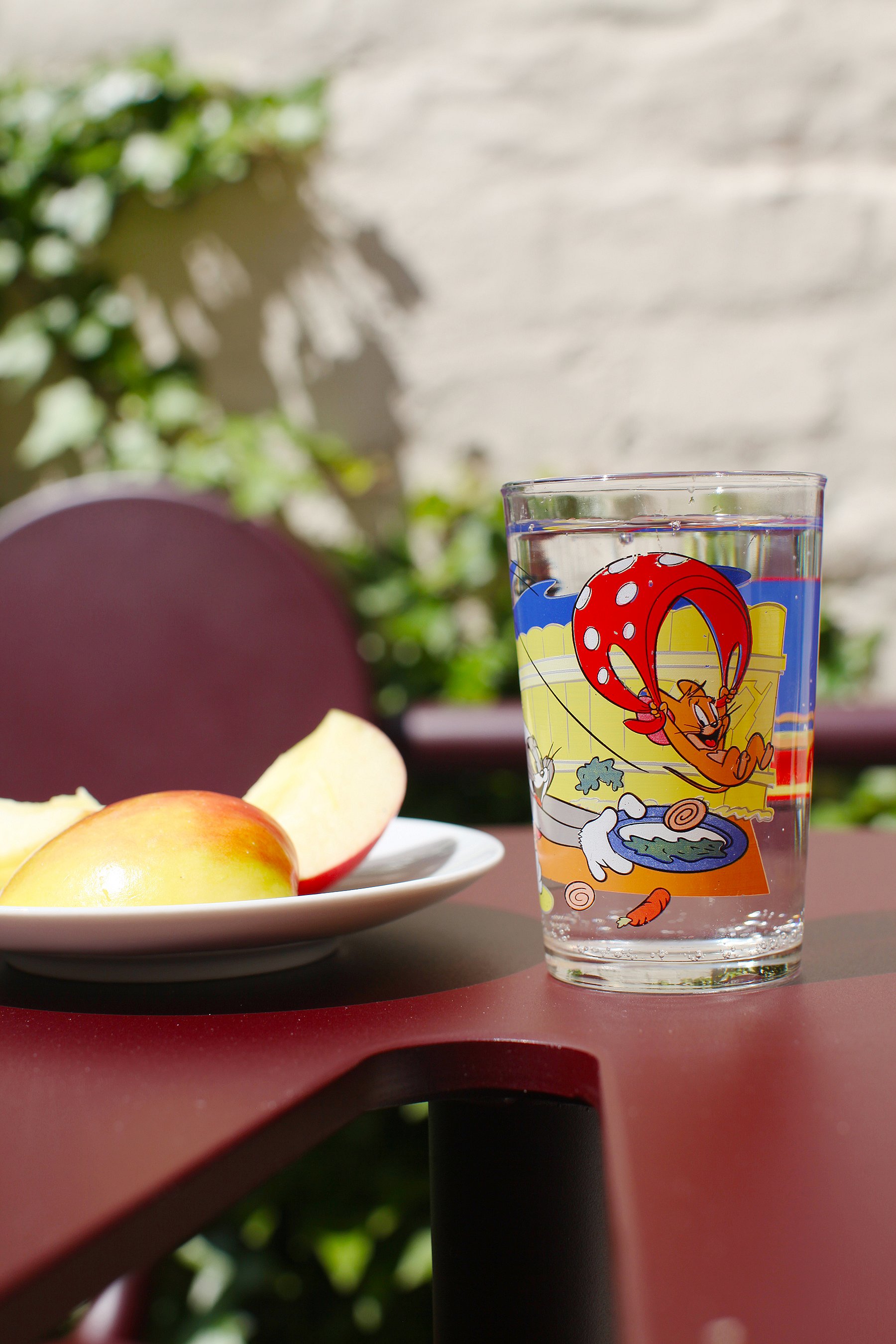   Detailansicht eines roten Bistrotisches auf einer gemütlichen Terrasse mit Getränken und kleinen Snacks für entspannte Momente in der Sonne.