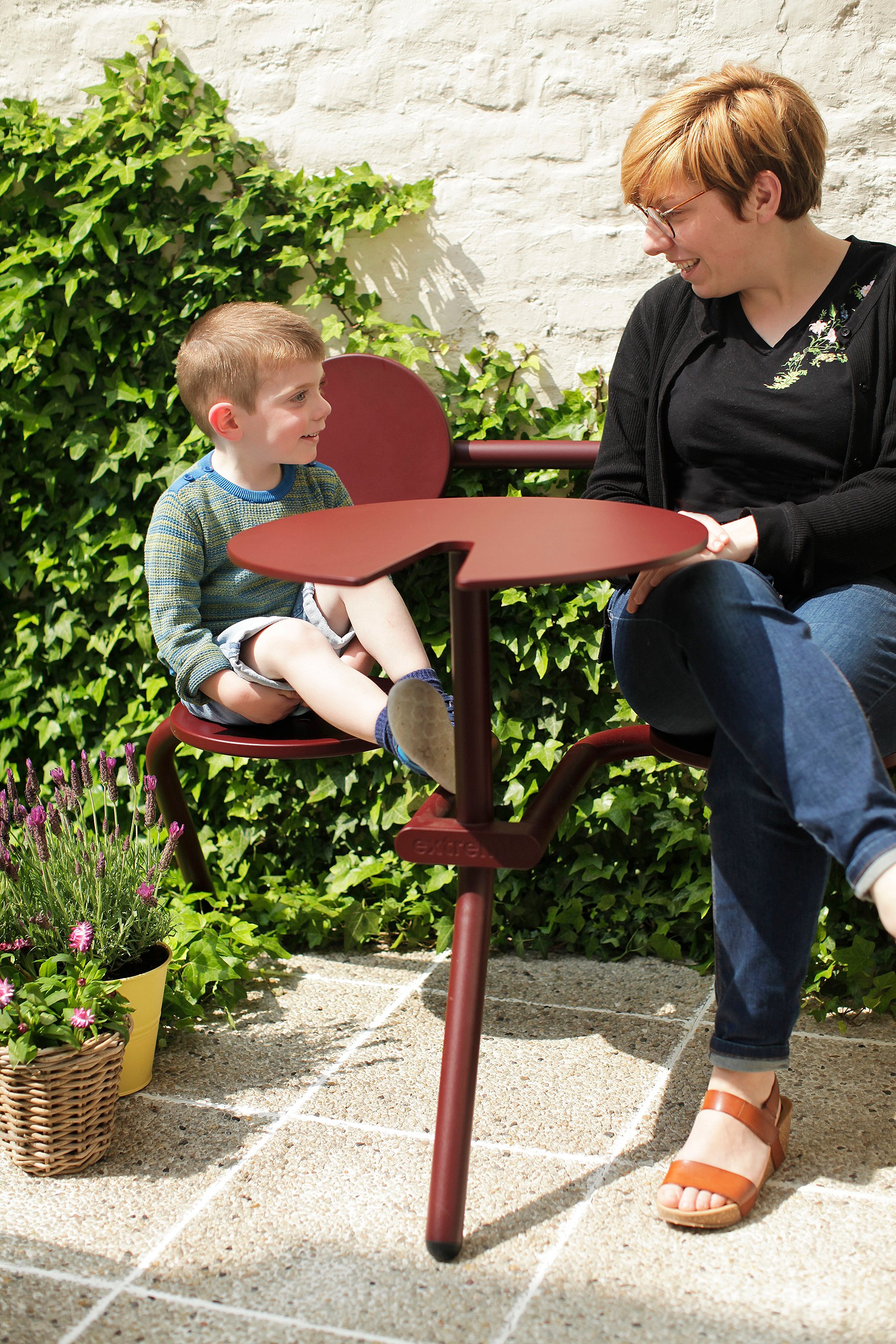   Kompakte Stadtterrasse mit rotem Bistrotisch, umgeben von Blumentöpfen und einem vertikalen Garten mit üppigen Kletterpflanzen.