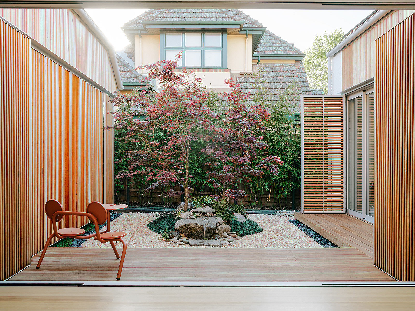 Ein mit Holz verkleideter Innenhof eines minimalistischen Hauses in Melbourne mit einem japanischen Ahornbaum im Zentrum und einer kupferbraunen Bistro-Tischgruppe auf der Terrasse.
