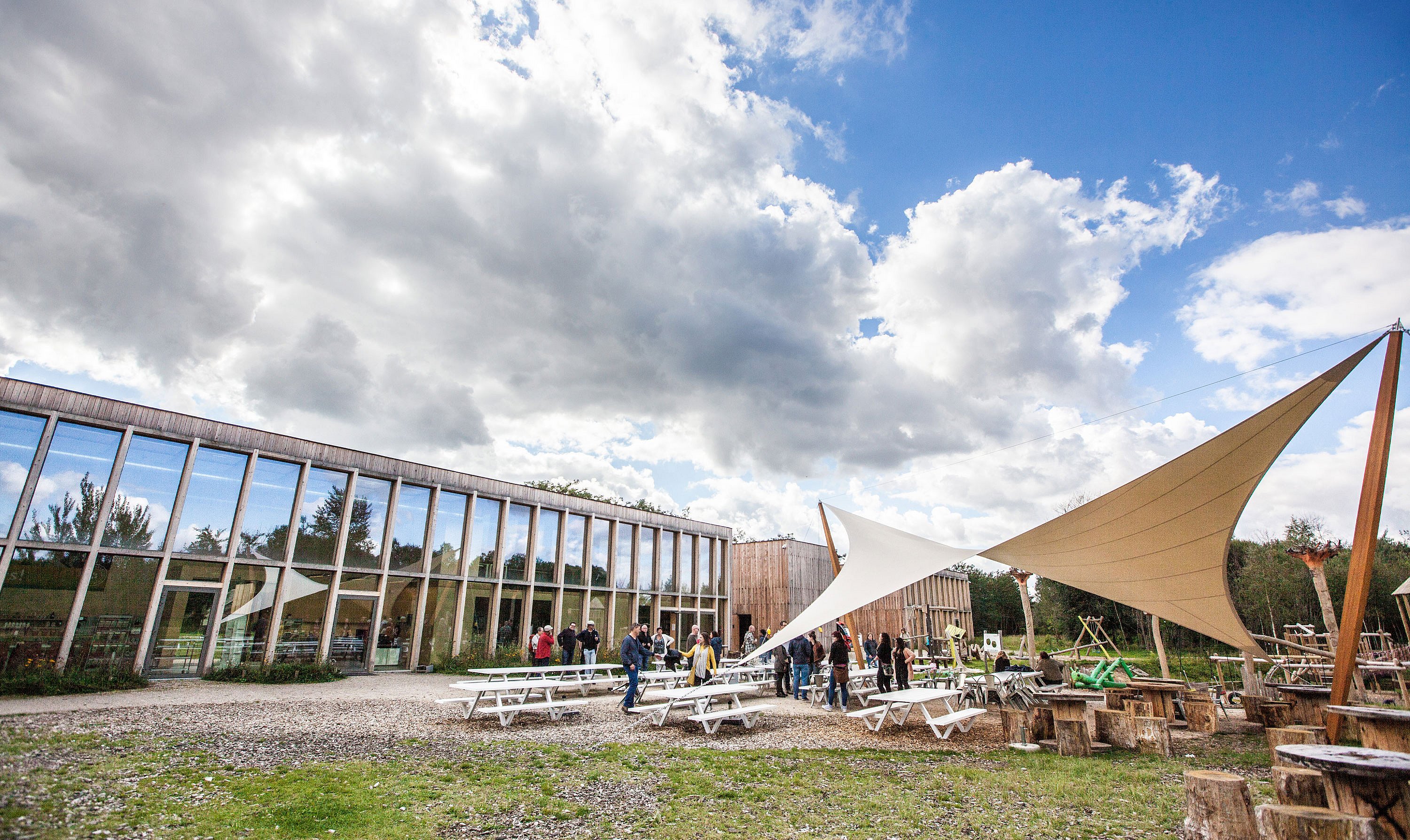   Bezoekers verzamelen zich rond de Marina-picknicktafels op het terras van Connecterra, waardoor een levendige ontmoetingsplek ontstaat bij de toegangspoort tot het nationale park.