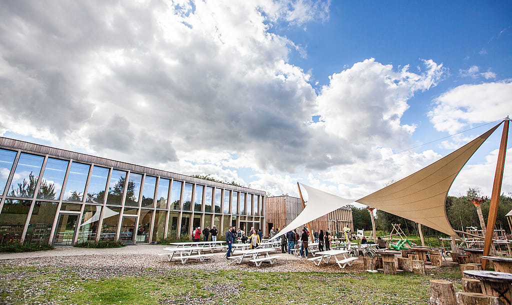 Bezoekers verzamelen zich rond de Marina-picknicktafels op het terras van Connecterra, waardoor een levendige ontmoetingsplek ontstaat bij de toegangspoort tot het nationale park.