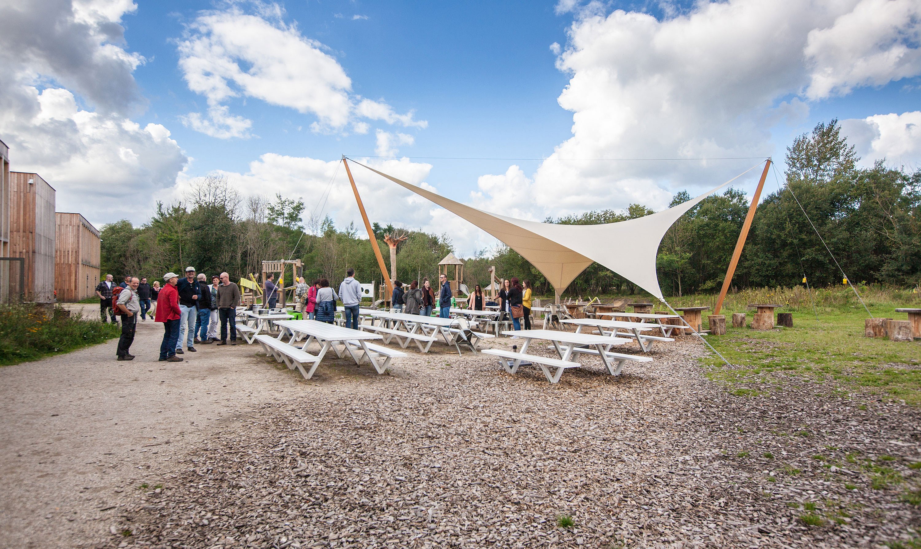   Ruim terras van Connecterra met Marina-picknicktafels en -banken, omgeven door bomen en groen vlakbij de ingang van het park.