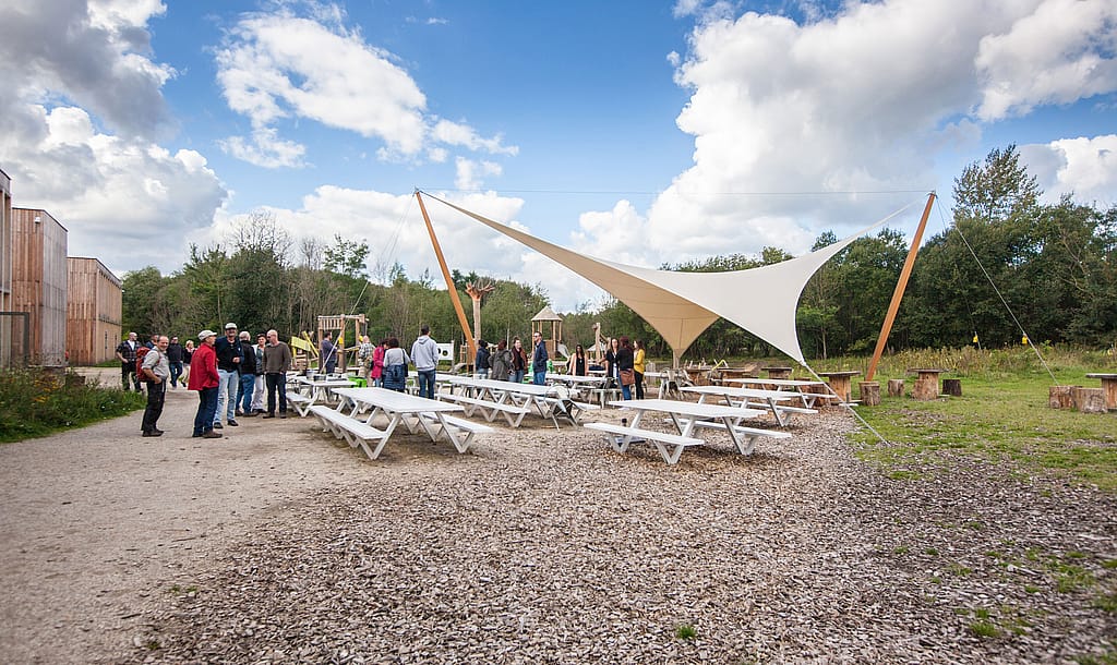 Ruim terras van Connecterra met Marina-picknicktafels en -banken, omgeven door bomen en groen vlakbij de ingang van het park.