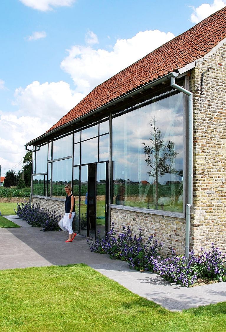   Der helle Innenraum des Ferienhauses mit Glasfront bietet Einblicke in die freiliegenden Holzbalken des Dachstuhls und einen weiten Blick in den umliegenden Garten.