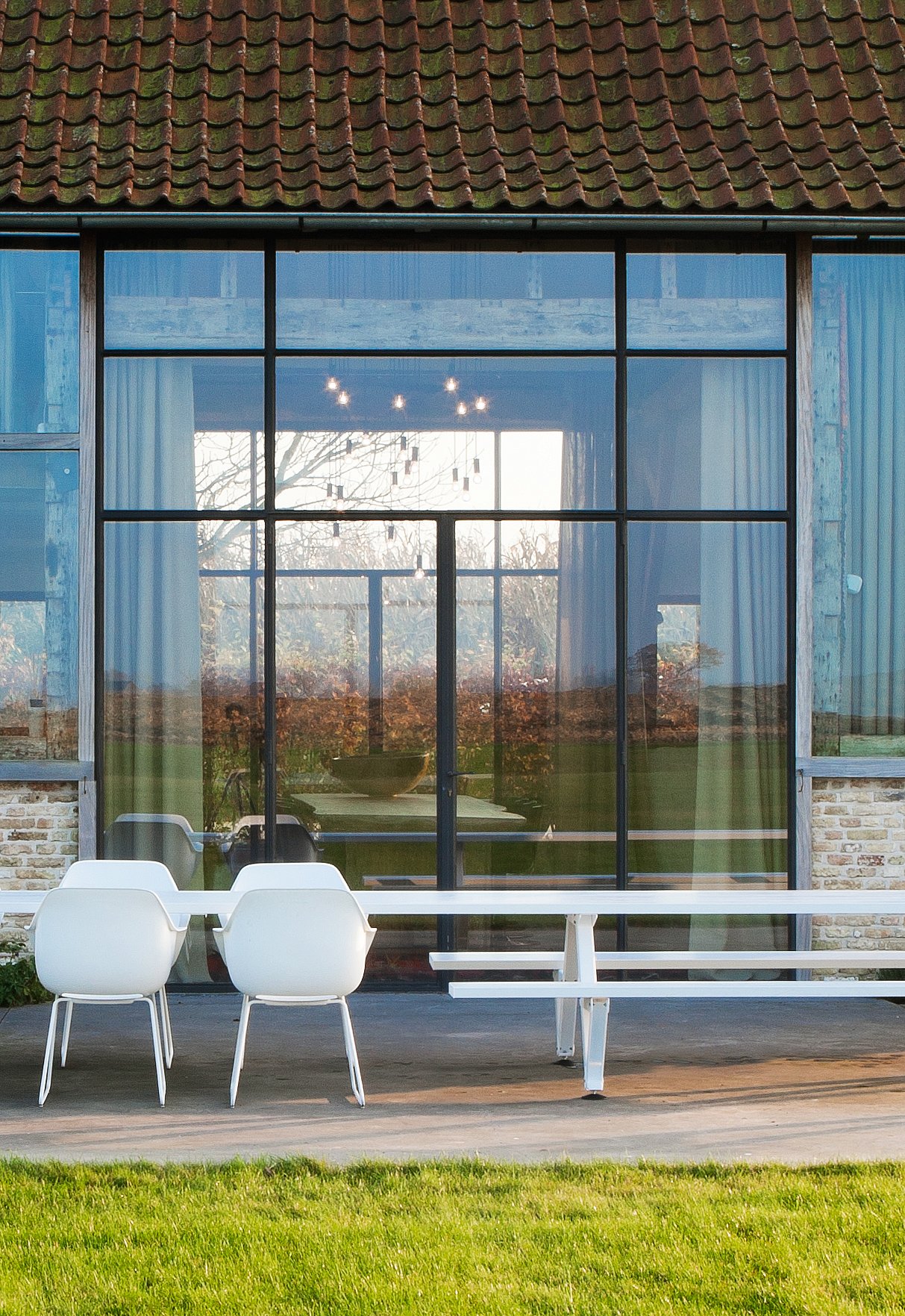   Die Terrasse mit einem langen Marina-Kombinationstisch, umgeben von Kapitänsstühlen und Bänken, befindet sich neben den großen Glasschiebetüren der renovierten Scheune.
