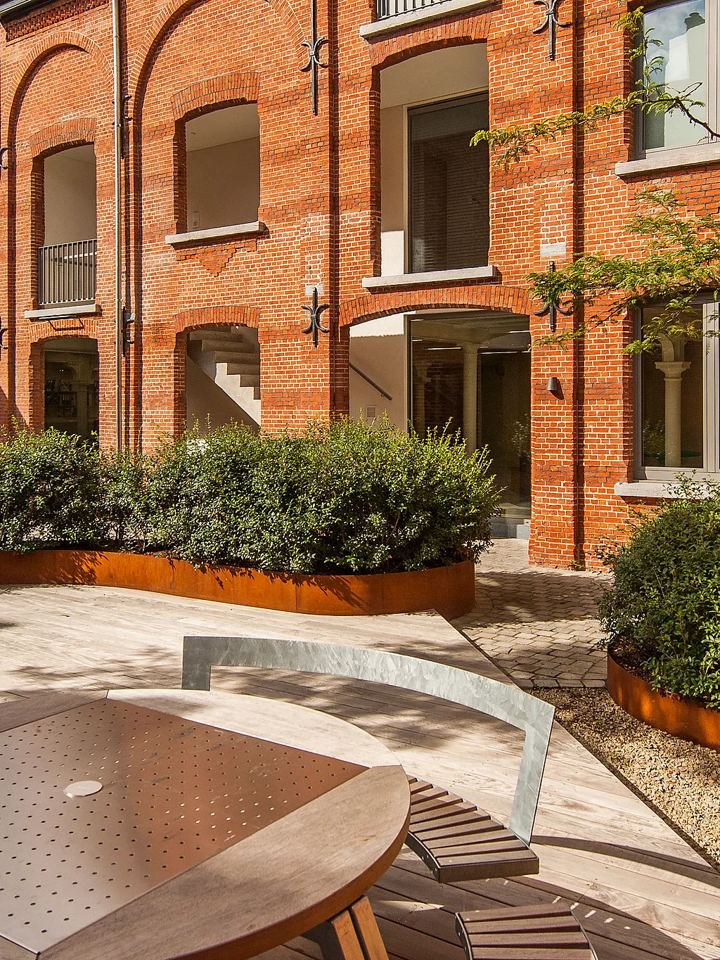 Historic brick sugar factory building converted into modern housing and workspaces, with balconies overlooking a landscaped courtyard garden with the Gargantua table.